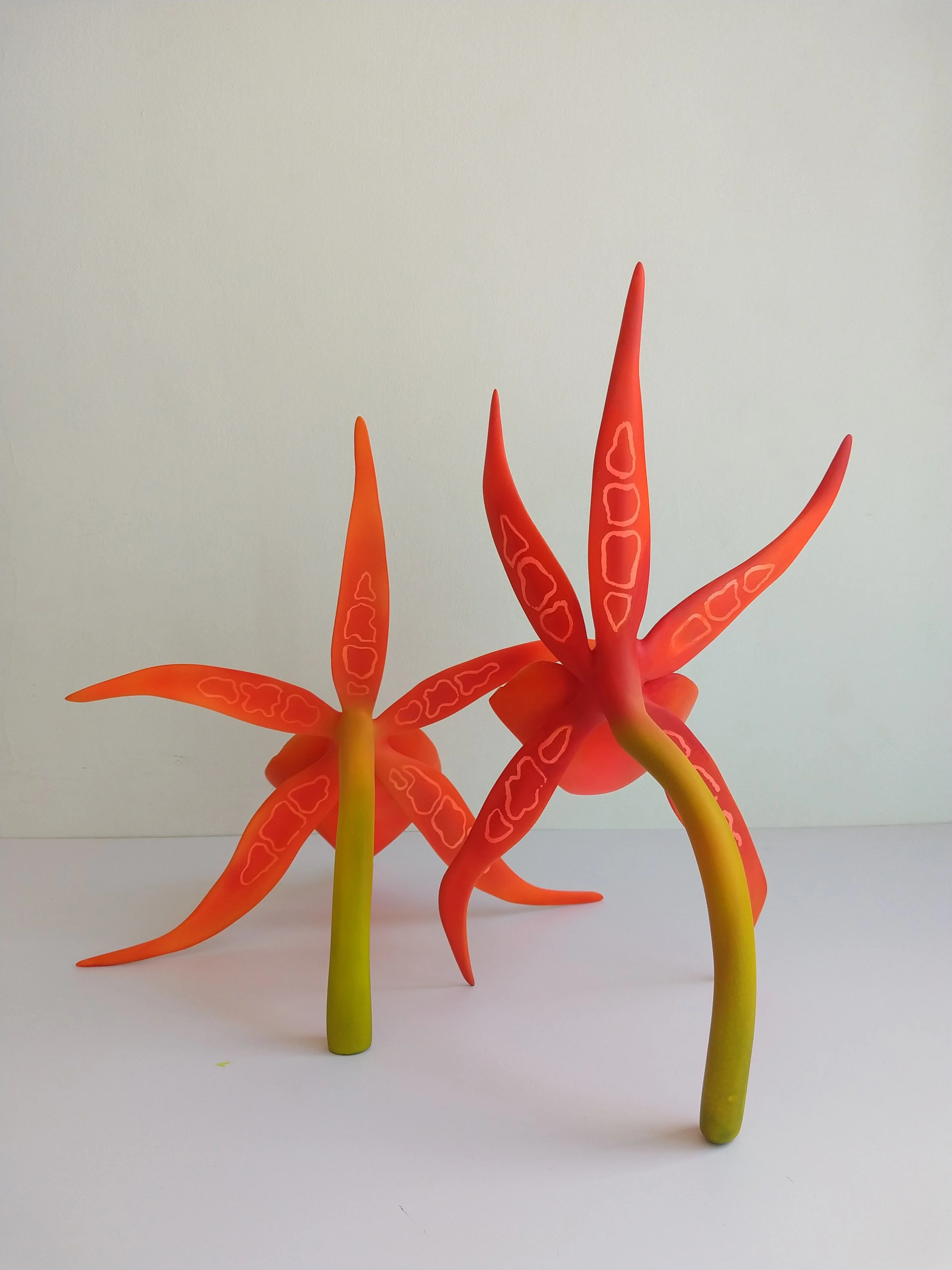 Colorful plastic toy plants with long, tapered leaves in red and yellow, set against a plain white background.