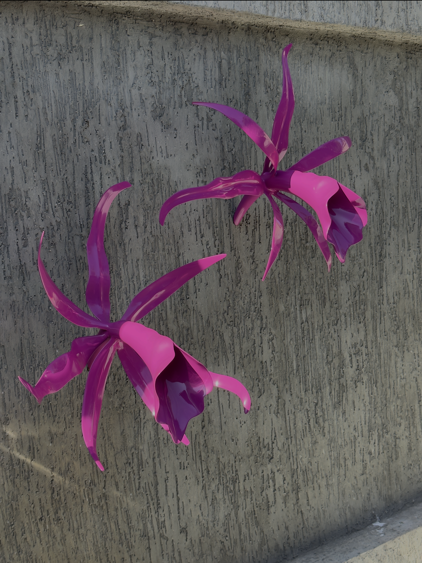 Pink glass sculpture resembling a flower with elongated petals mounted on a textured gray stone wall.