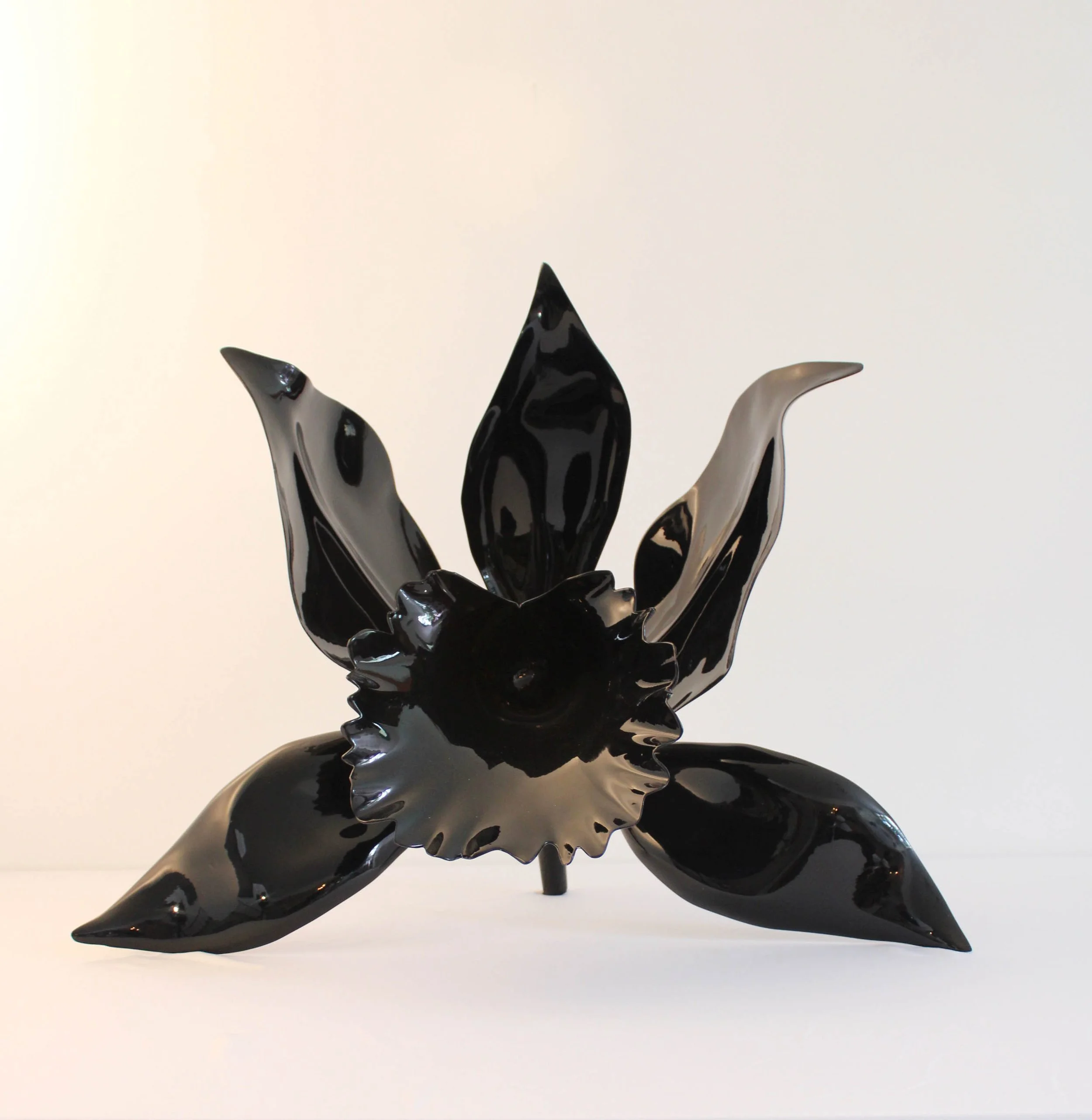Black and white glass sculpture resembling a flower or plant with elongated, curved petals and a glossy finish.