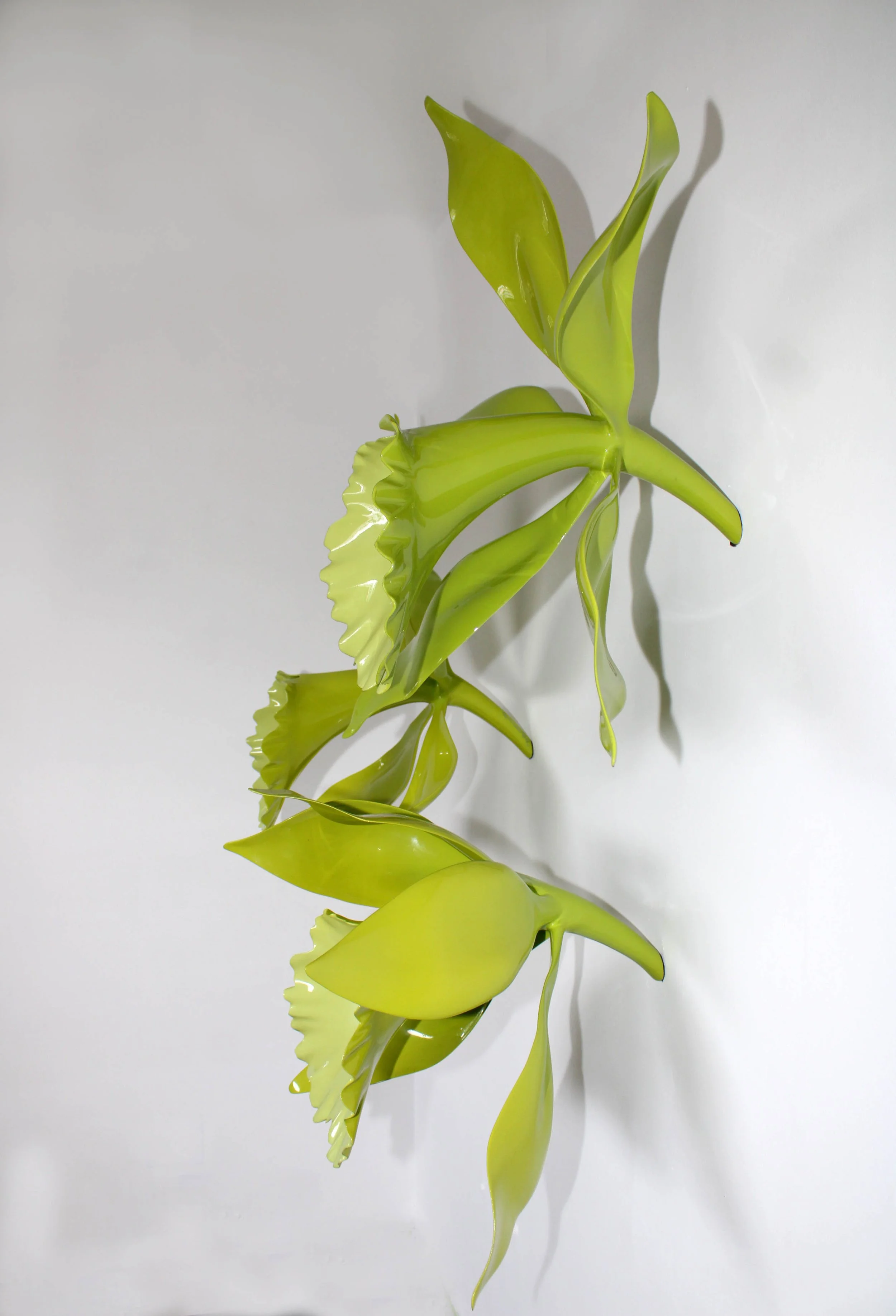 A yellowish-green, abstract, sculptural art piece resembling plant leaves against a plain white background.