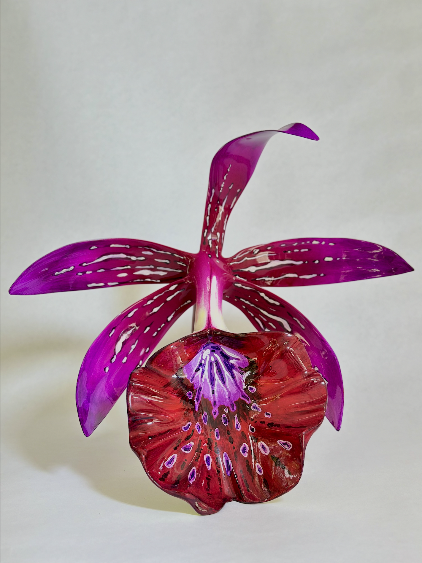 A colorful glass sculpture of a flower with pink, purple, and red petals set against a plain, light background.