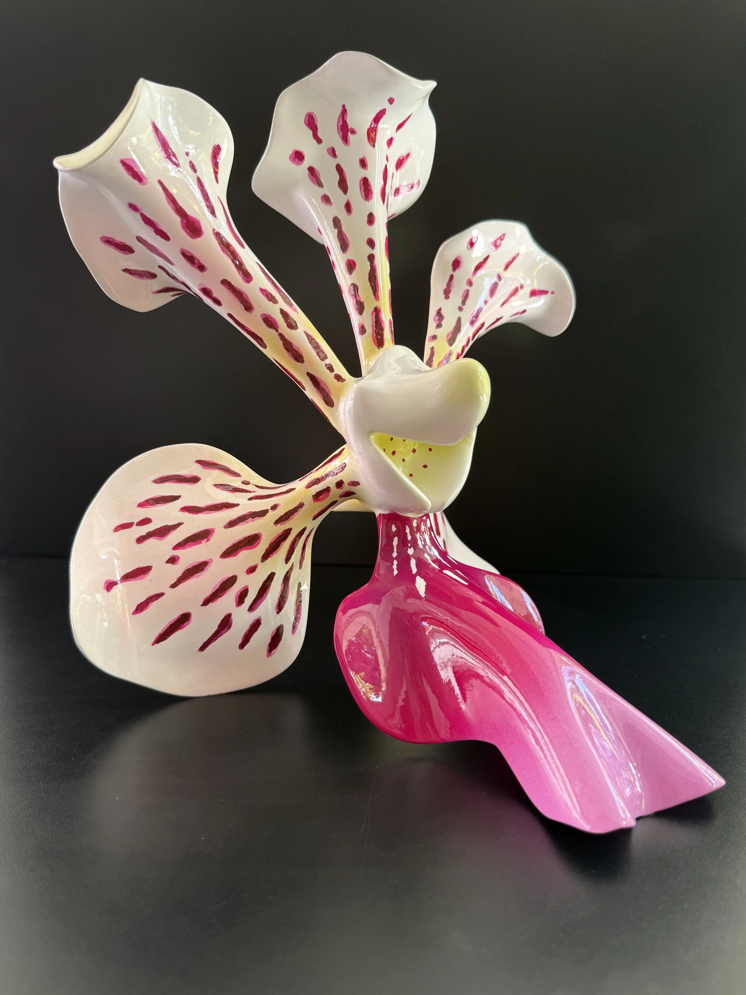A colorful glass sculpture of a flower with white petals with pink and yellow speckles and a bright pink stem, set against a black background.