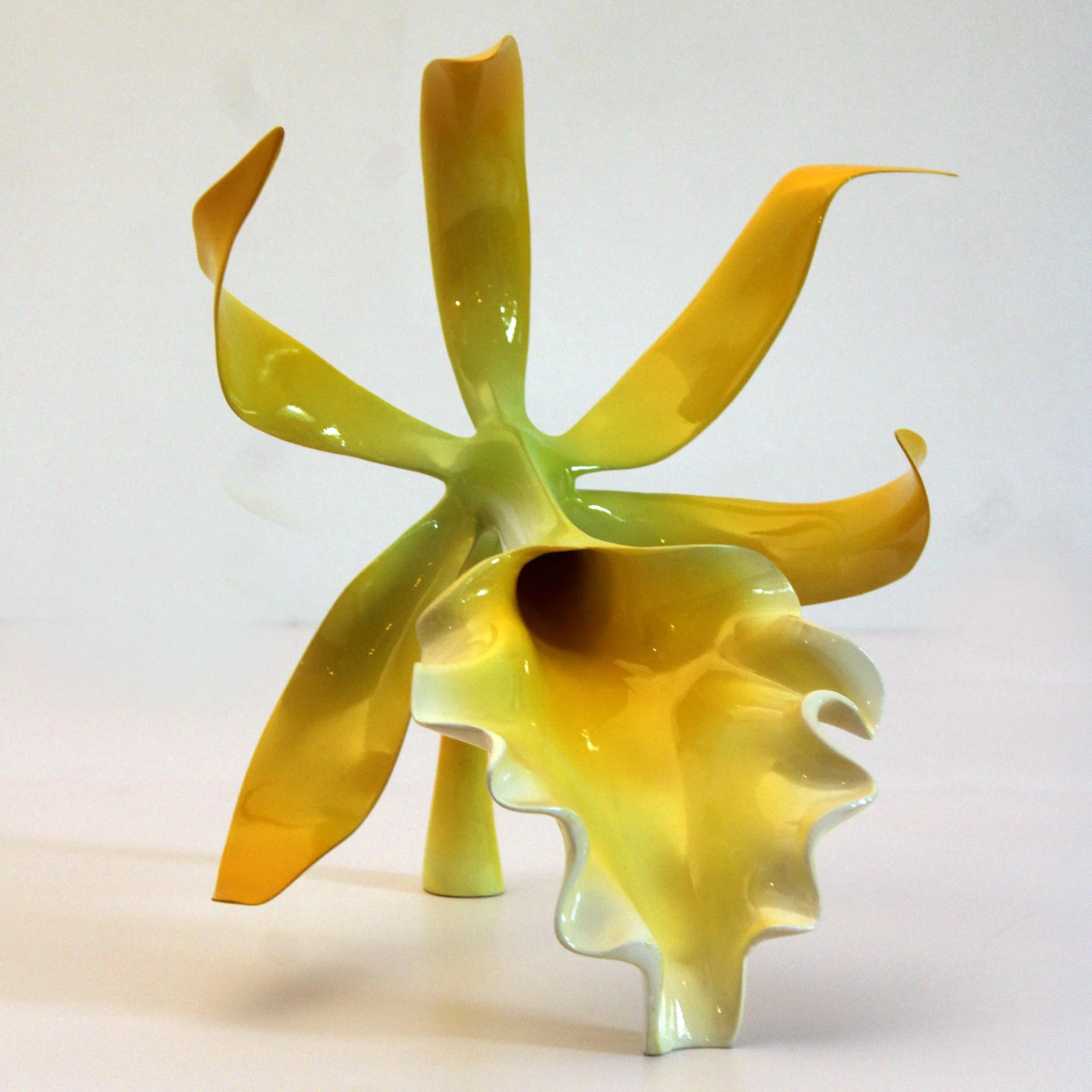 A yellow plastic sculpture resembling a stylized flower or plant with flowing, curved petals and a tall, central stem, set against a plain white background.