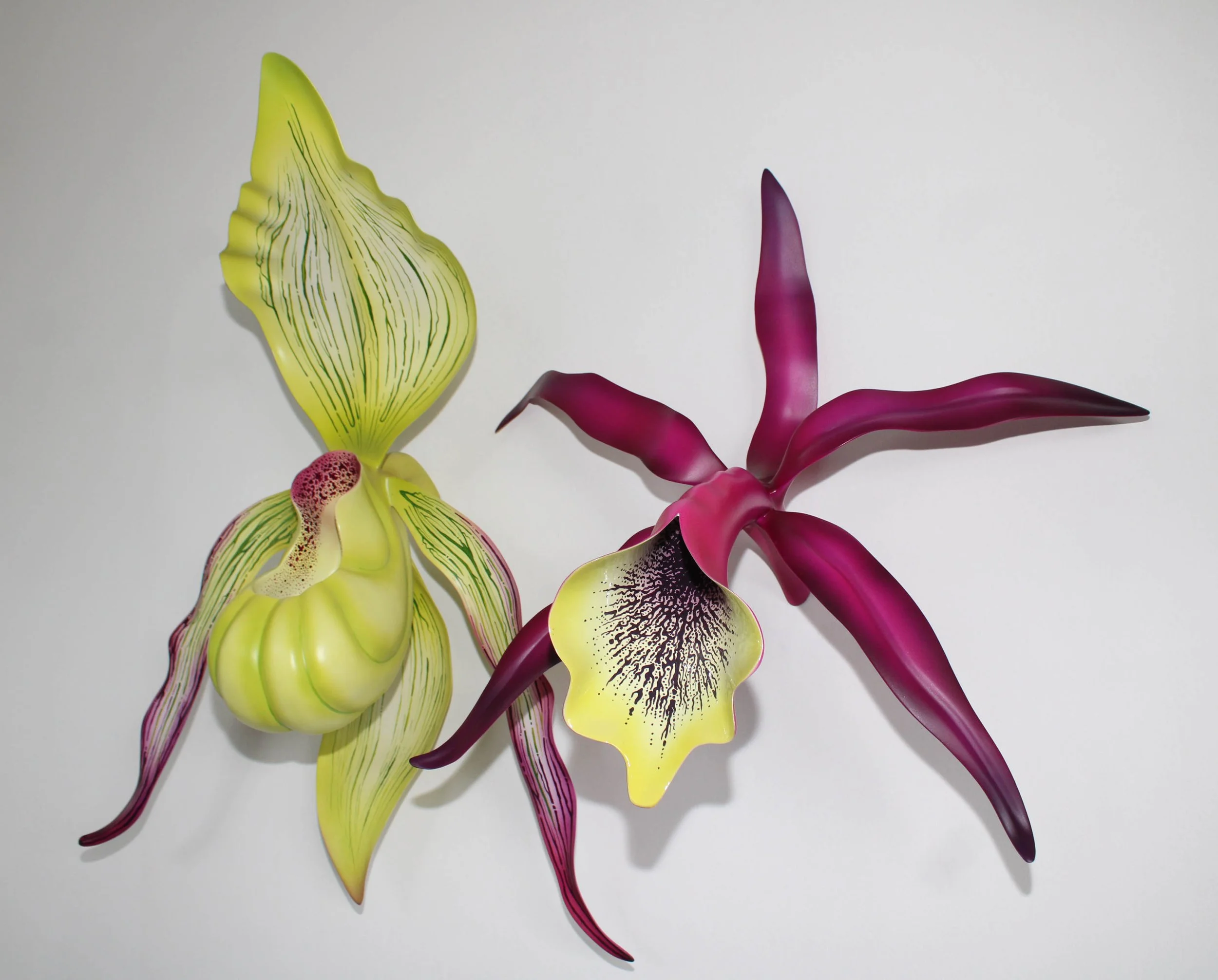 Three decorative orchid flowers, one yellow and green, one pink and purple, on a plain white background.