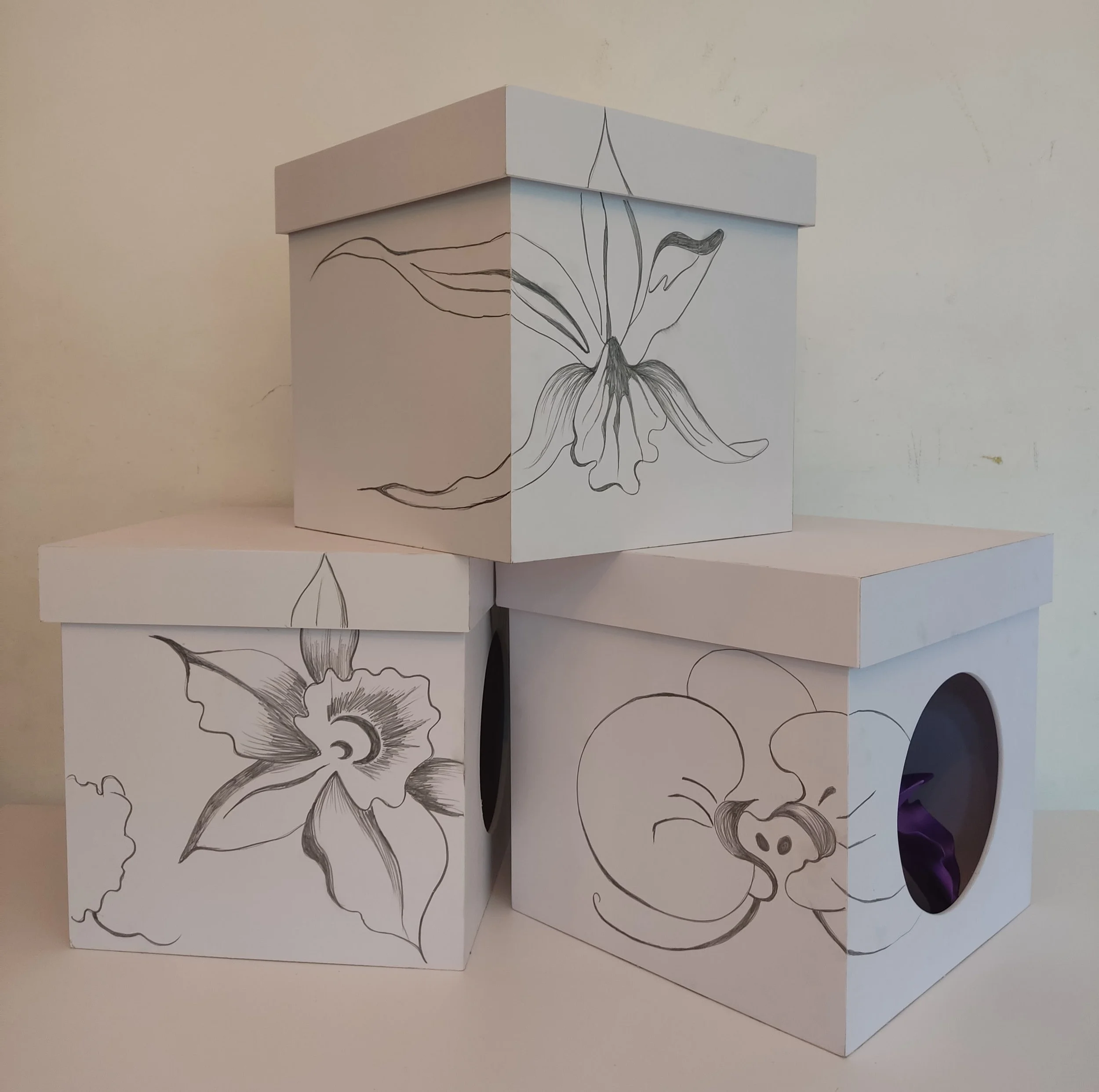 A white cardboard box with a black line drawing of a flower on its side, placed on a white surface against a plain light-colored wall.