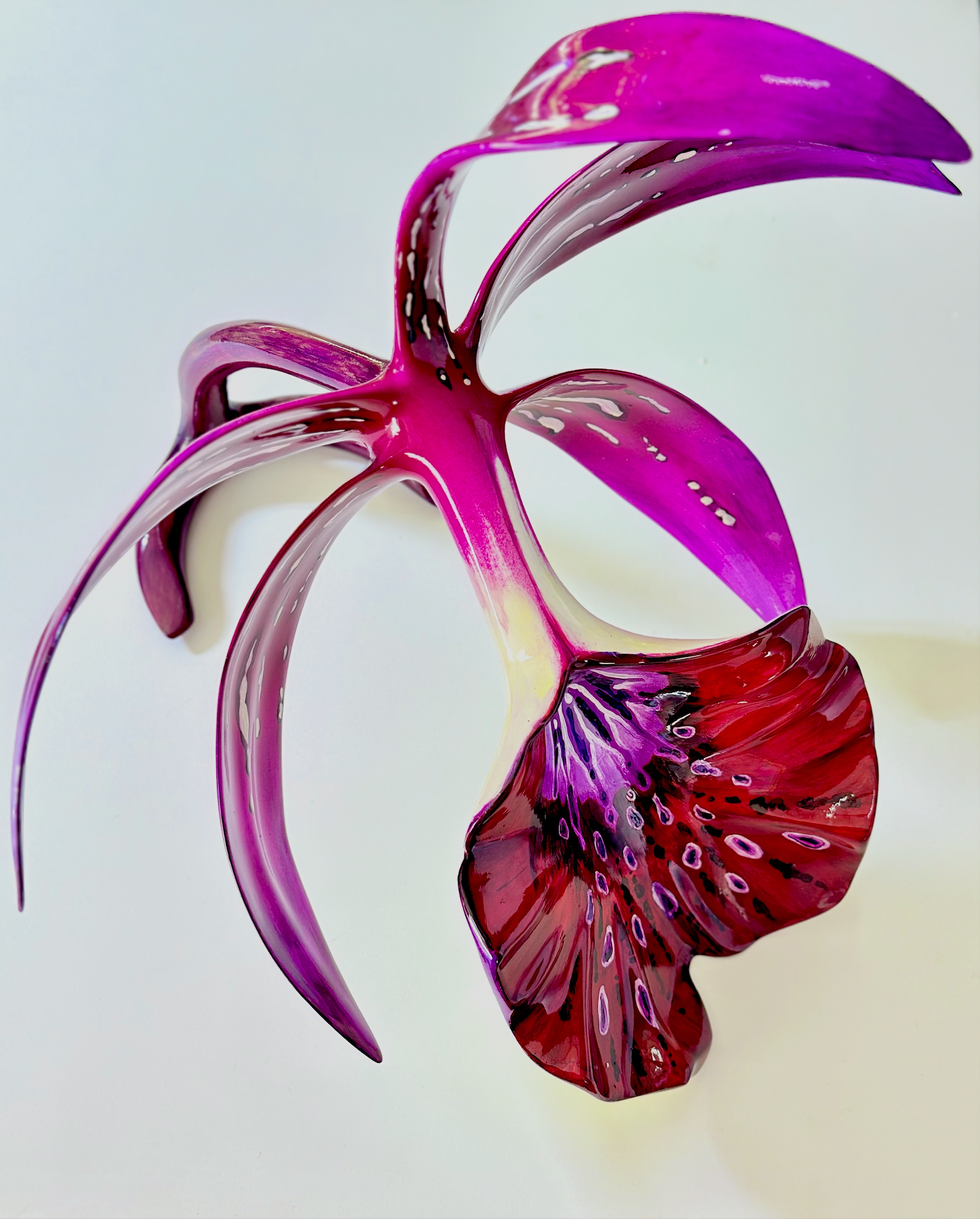 Close-up of a colorful glass sculpture resembling a floral design with pink, purple, red, and white hues, set against a plain background.