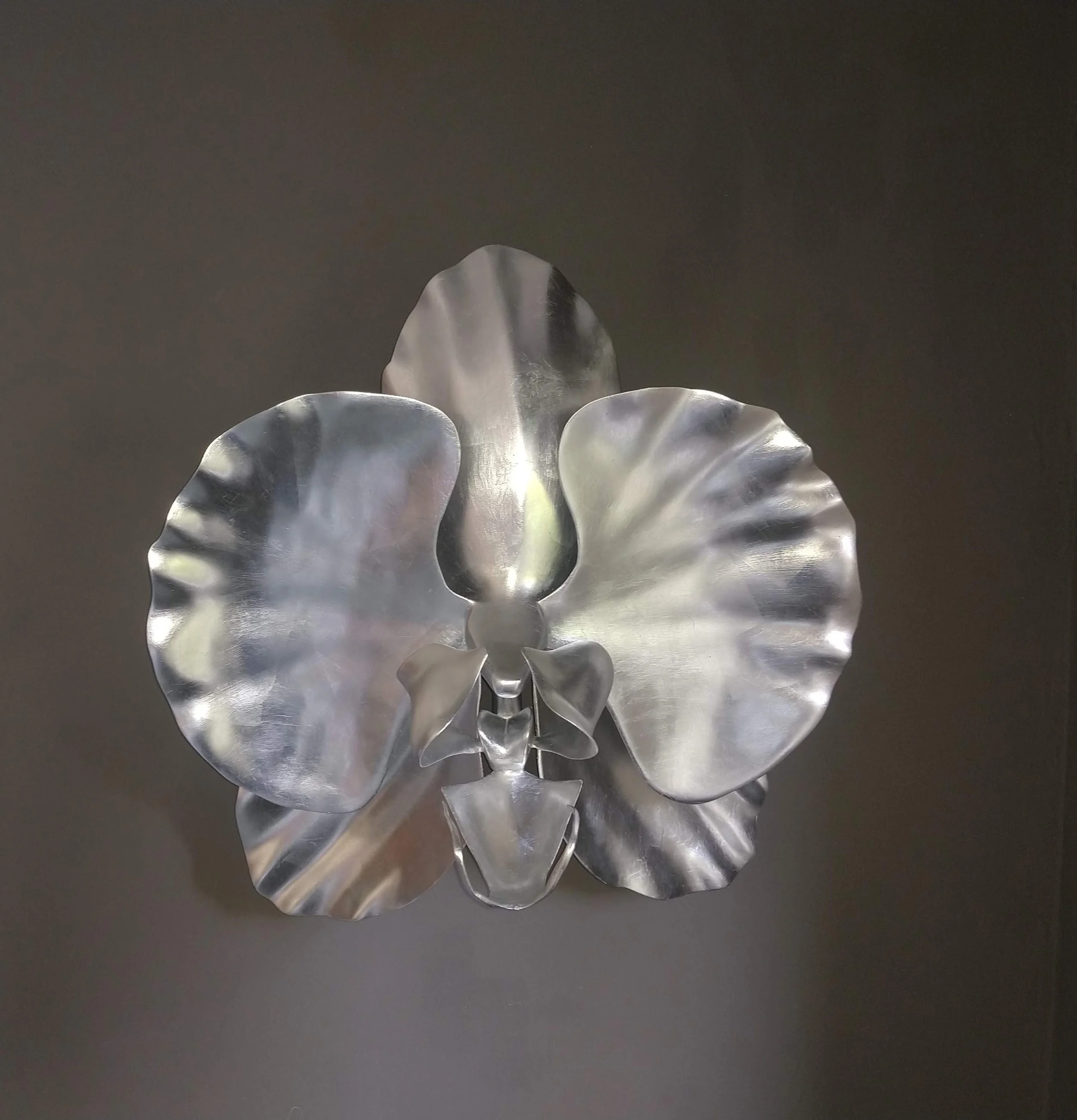 Close-up of a metallic flower sculpture with reflective, shiny petals set against a dark background.