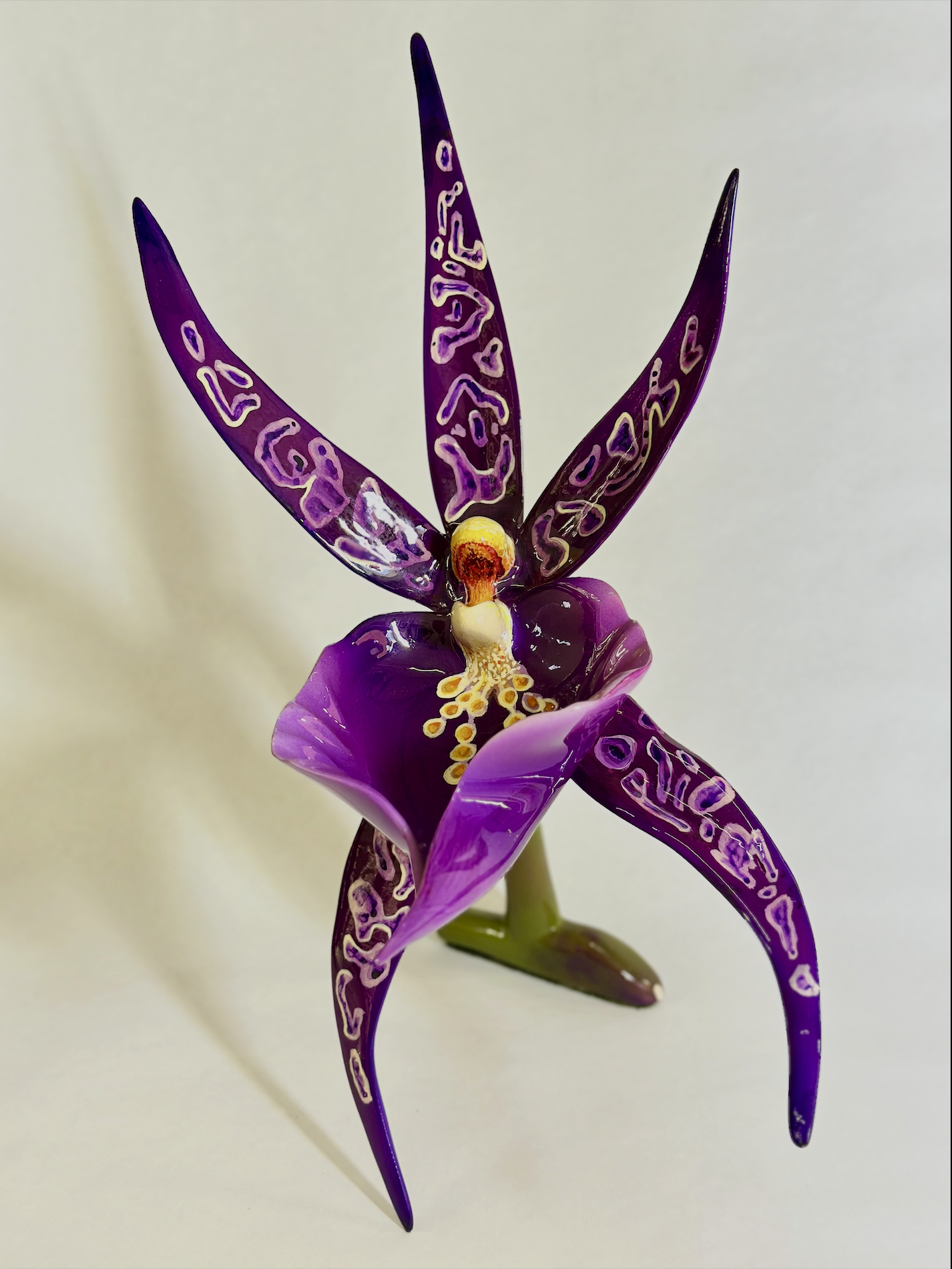 A vibrant purple orchid flower with intricately patterned petals and a yellow and white center, set against a plain background.
