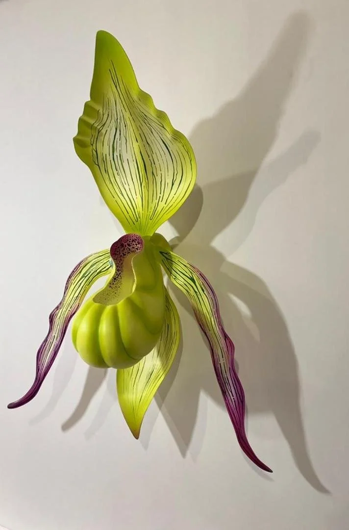 A decorative sculpture of a flower with green, purple, and yellow petals casting a shadow against a white background.