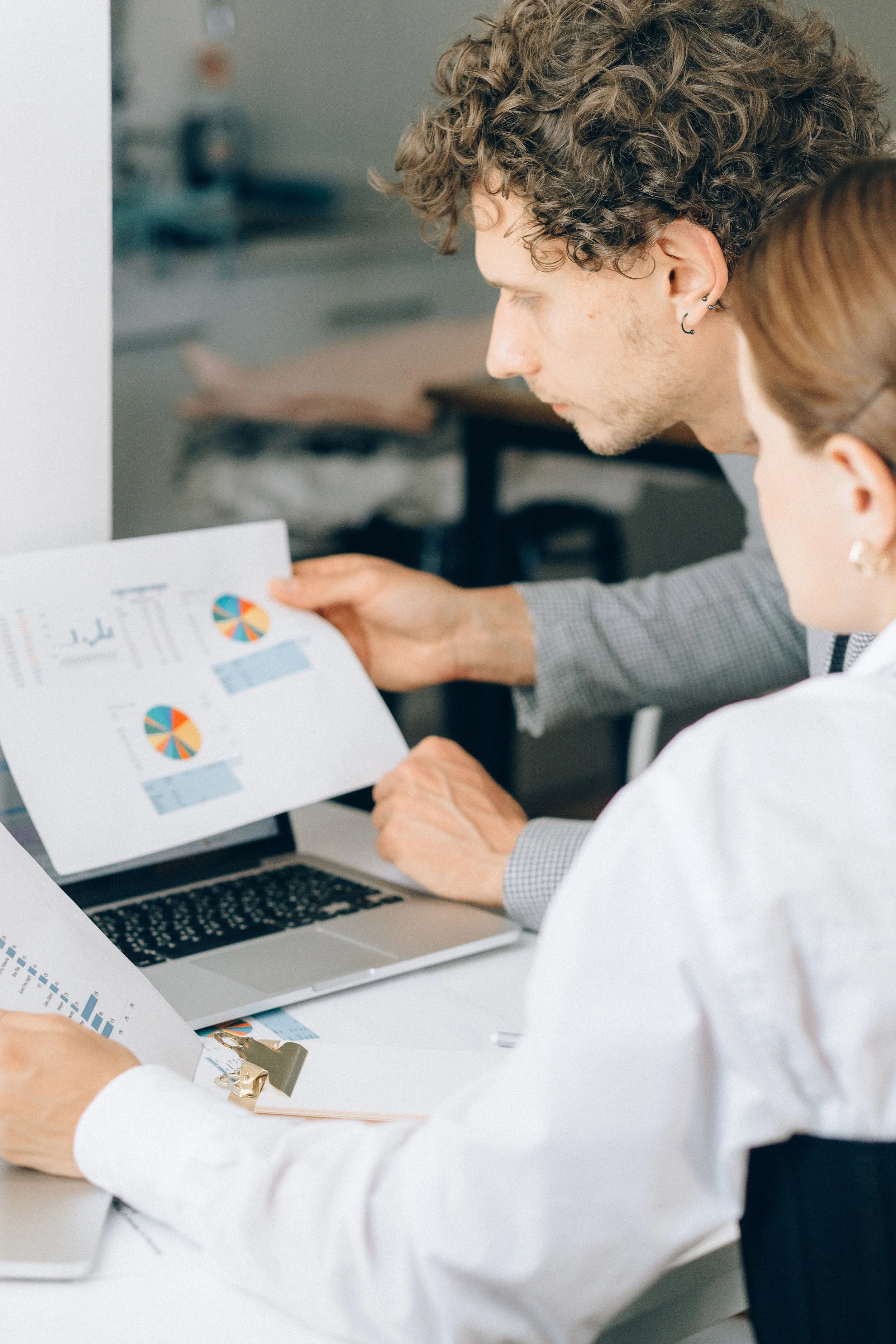 Two individuals reviewing financial charts and graphs, with a laptop open on a desk, in an office setting.