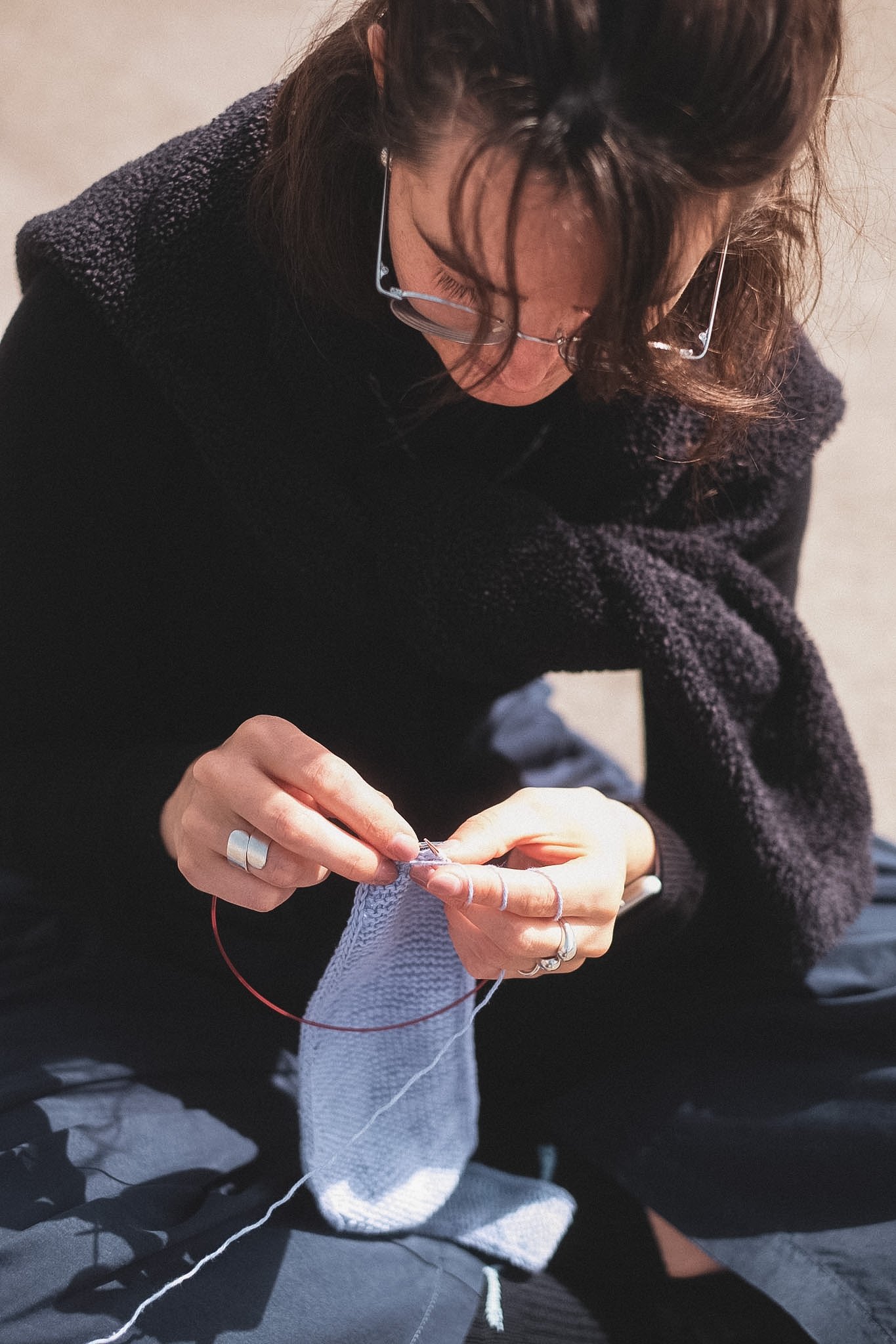Frau mit Brille strickt mit Rundstricknadeln an einem violetten "Sophie" Scarf von Petite Knit.