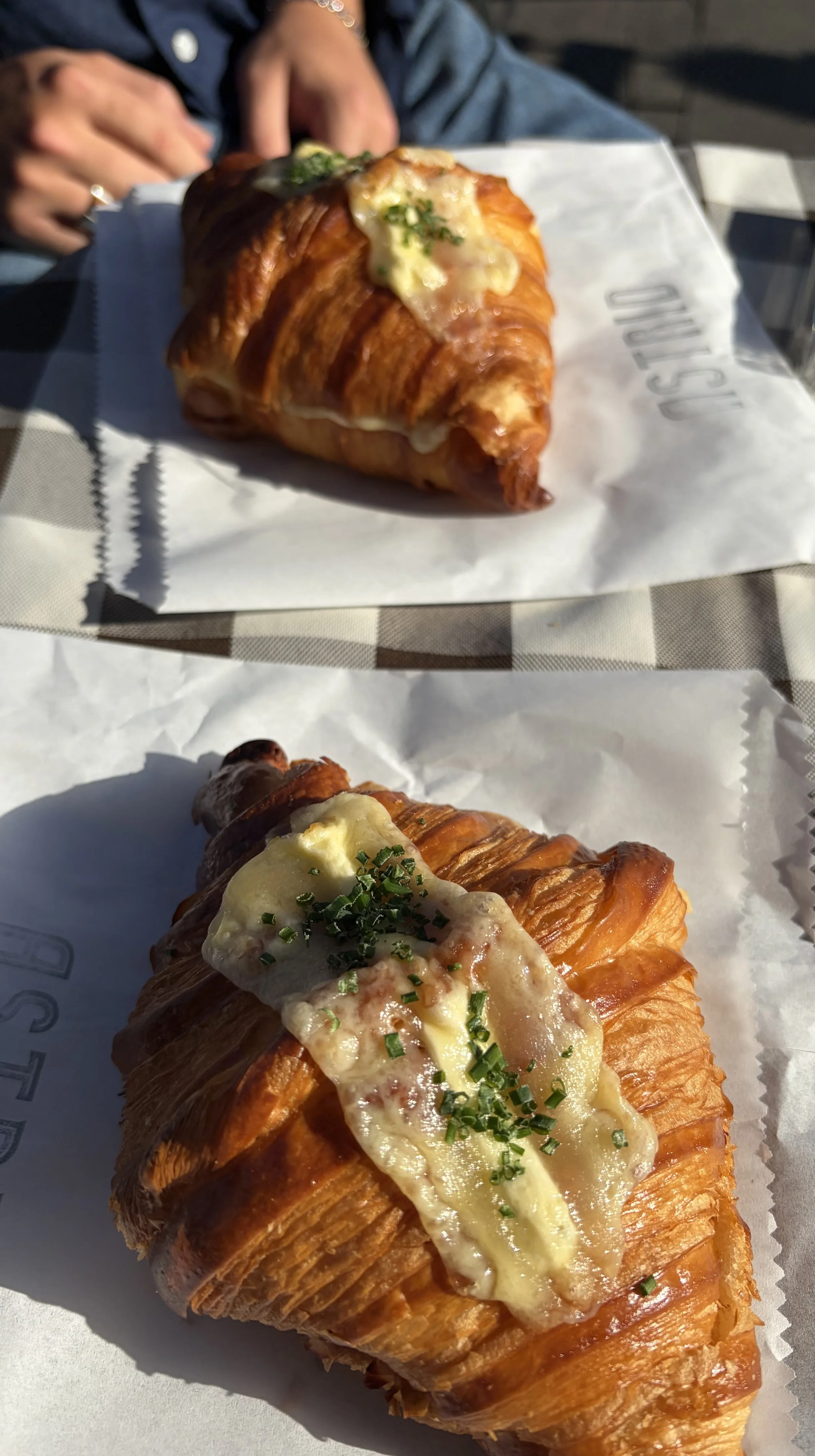 Two croissants topped with melted cheese and chopped chives, served on white paper.
