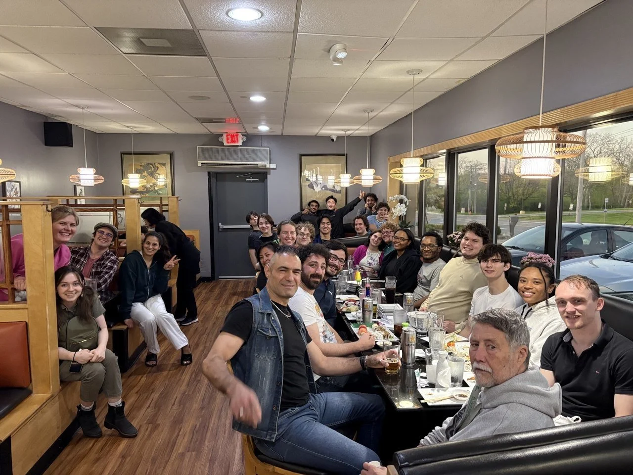 A large group of people sitting around a long table in a restaurant, smiling and enjoying a meal together.
