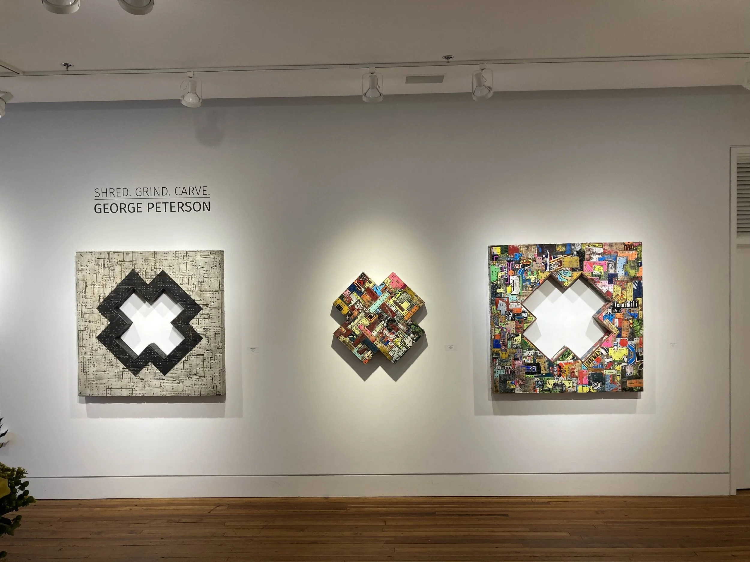 Three colorful abstract geometric artworks on a gallery wall, with a label that reads 'SHRED. GRIND. CARVE. GEORGE PETERSON'