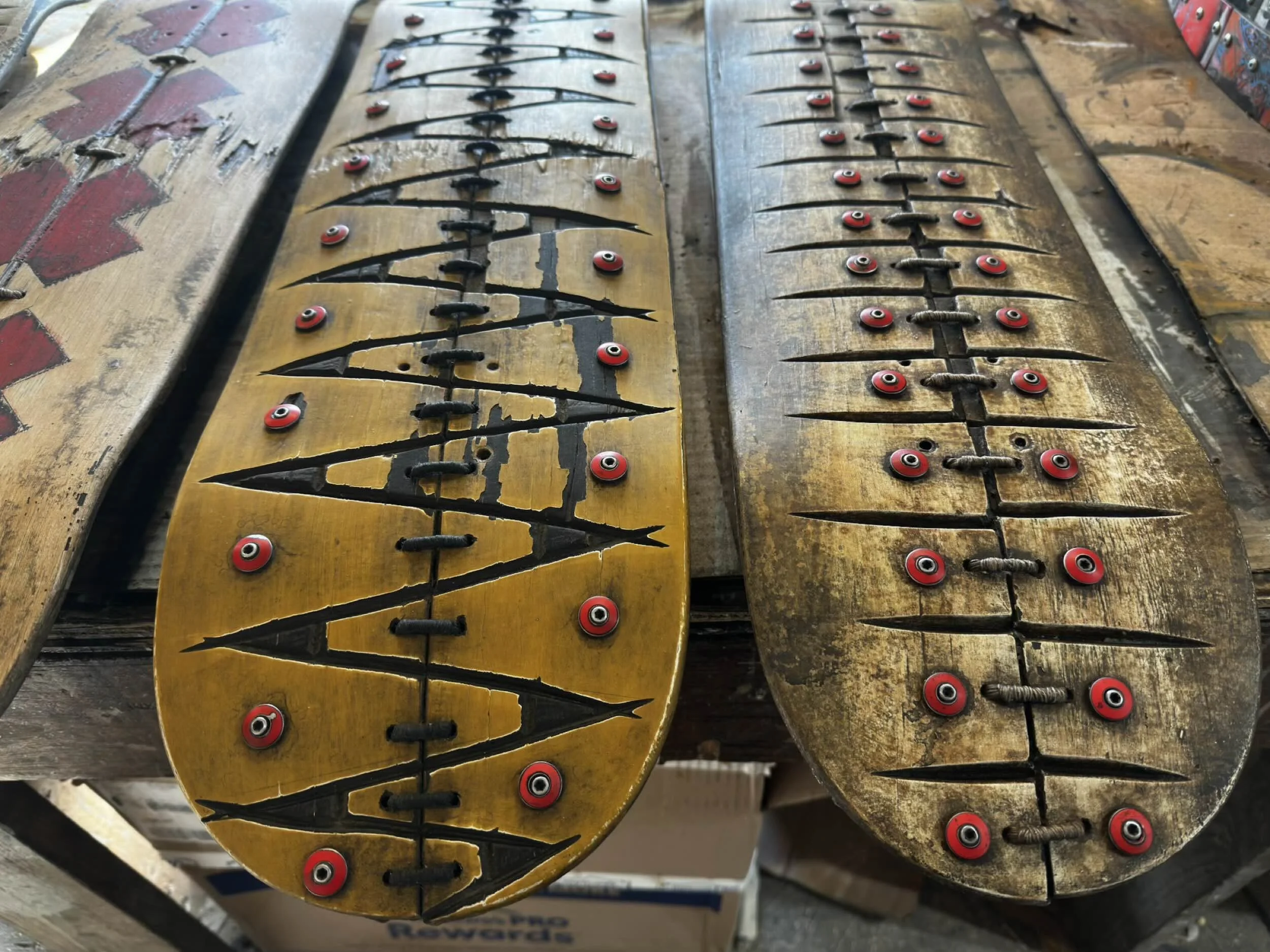 Close-up of three fine art gallery skateboards layered on top of each other with worn, cracked wooden decks, some with visible paint and scratches, and red and black wheels attached.