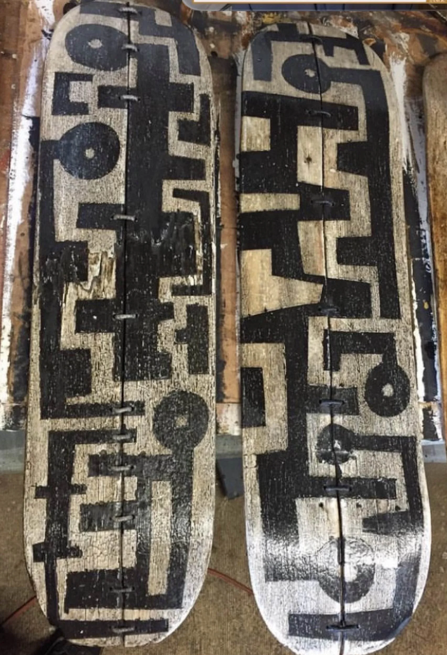 Two fine art skateboard sculpture shapes with painted in black on a white background, showing signs of wear and scratches.