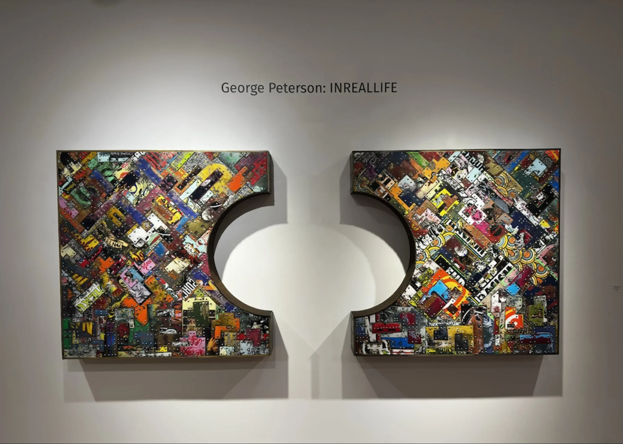 This image shows two large collage artworks mounted on a gallery wall beneath a sign that reads "George Peterson: INREALLIFE." Each collage is composed of numerous small, colorful images arranged in a mosaic pattern, with a partial, circular cutout i