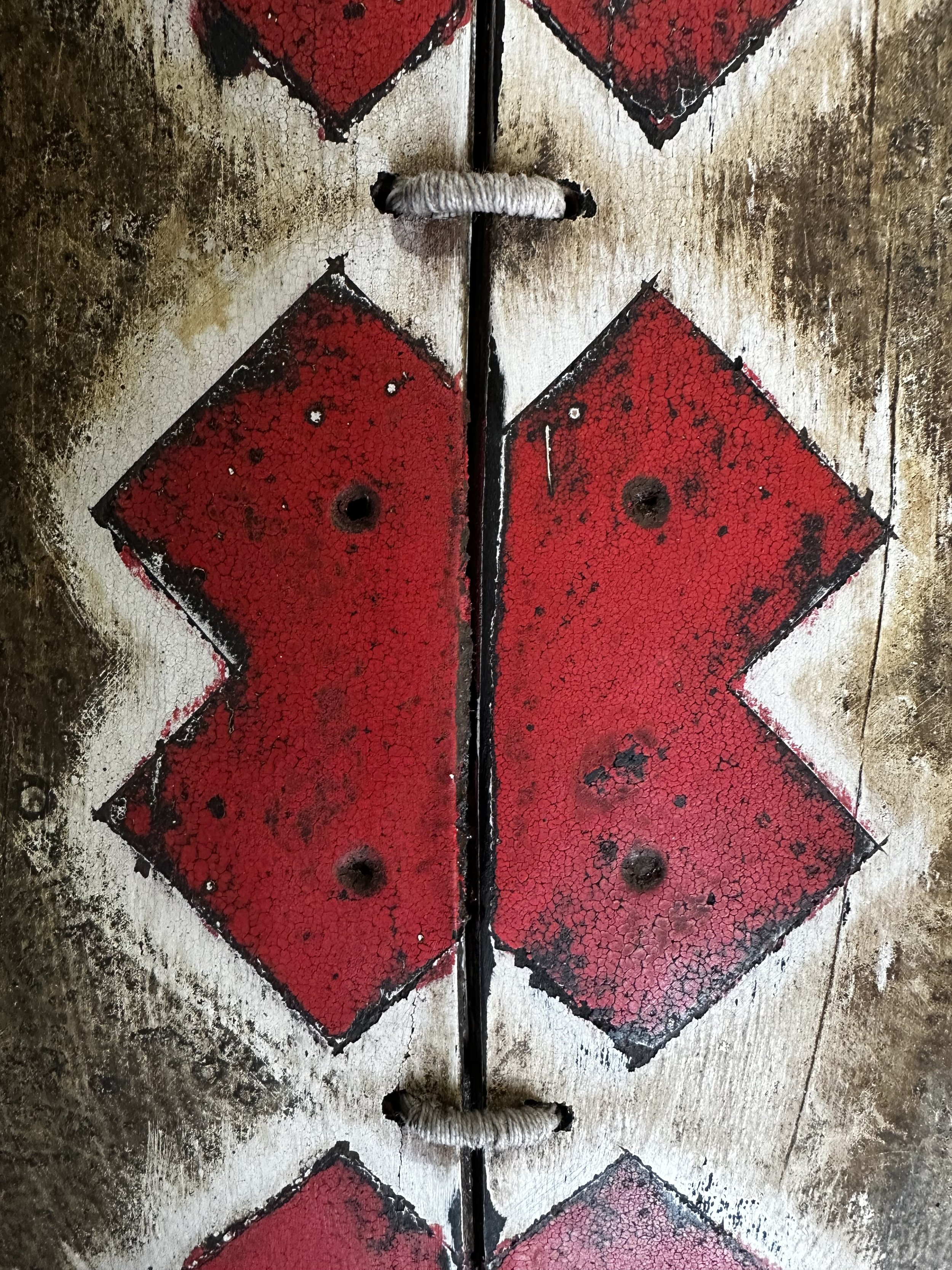 Close-up detail of hand-marked red X pattern and worn wood grain on George Peterson's LINGO Red X's wall sculpture.