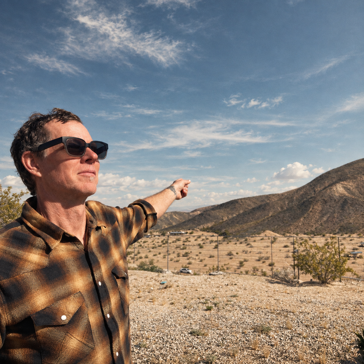 Man wearing sunglasses pointing at distant mountains in a desert landscape