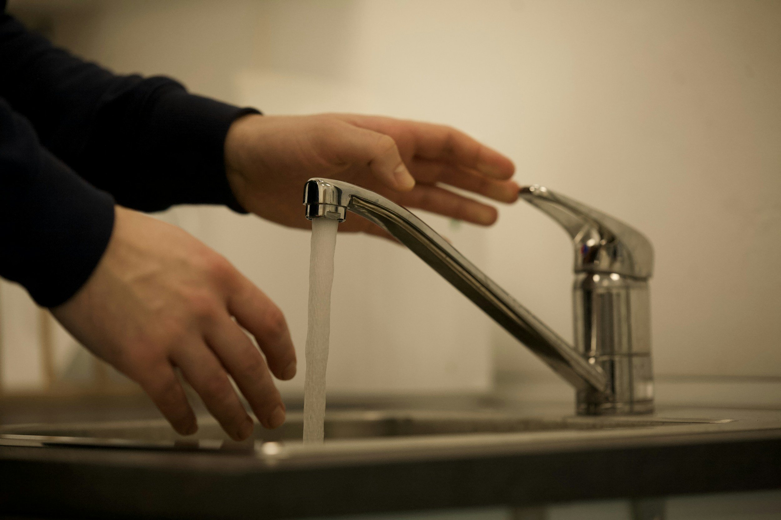 Person washing their hands under running water from a faucet.