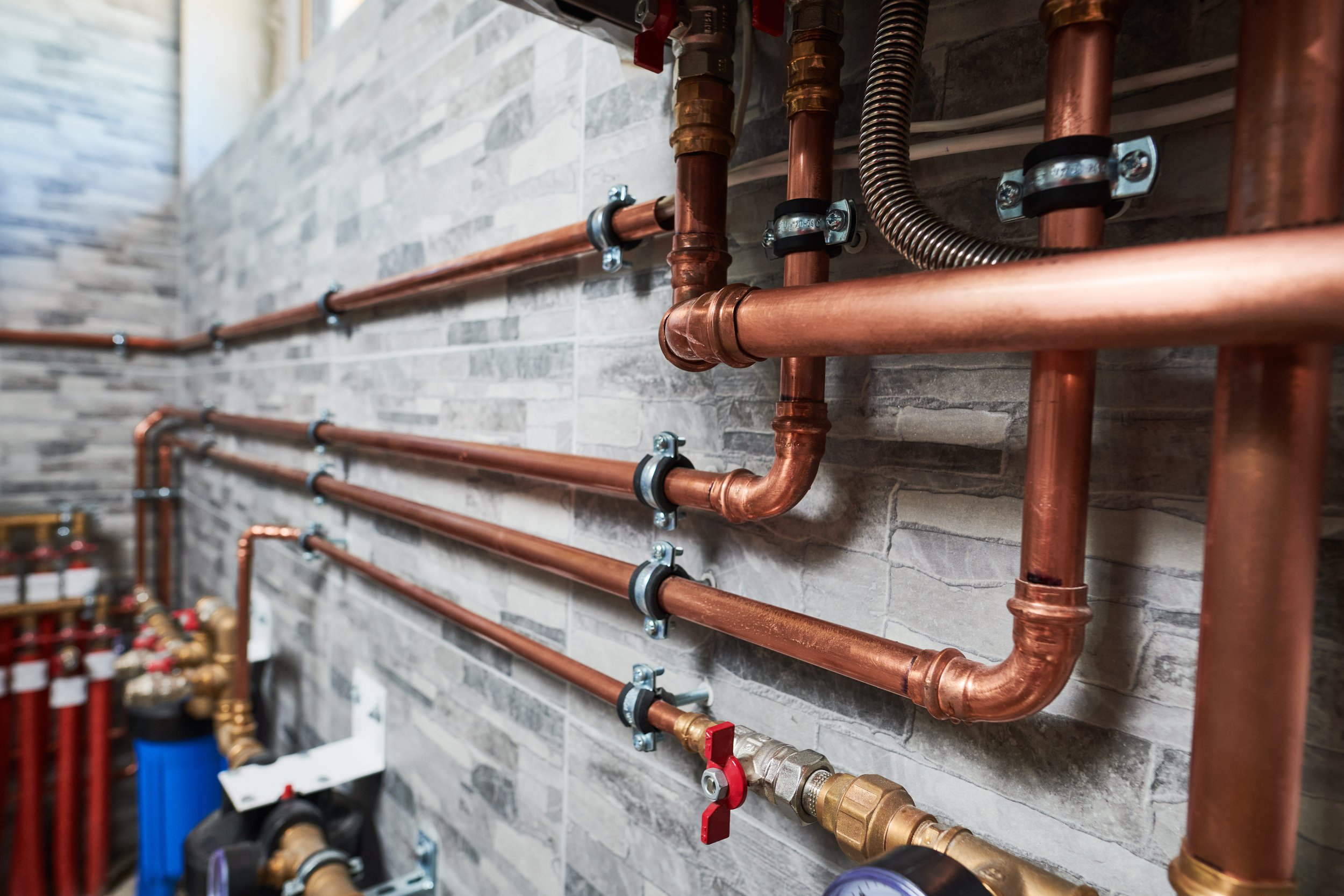 Copper plumbing pipes and fittings installed on a wall with metal brackets.
