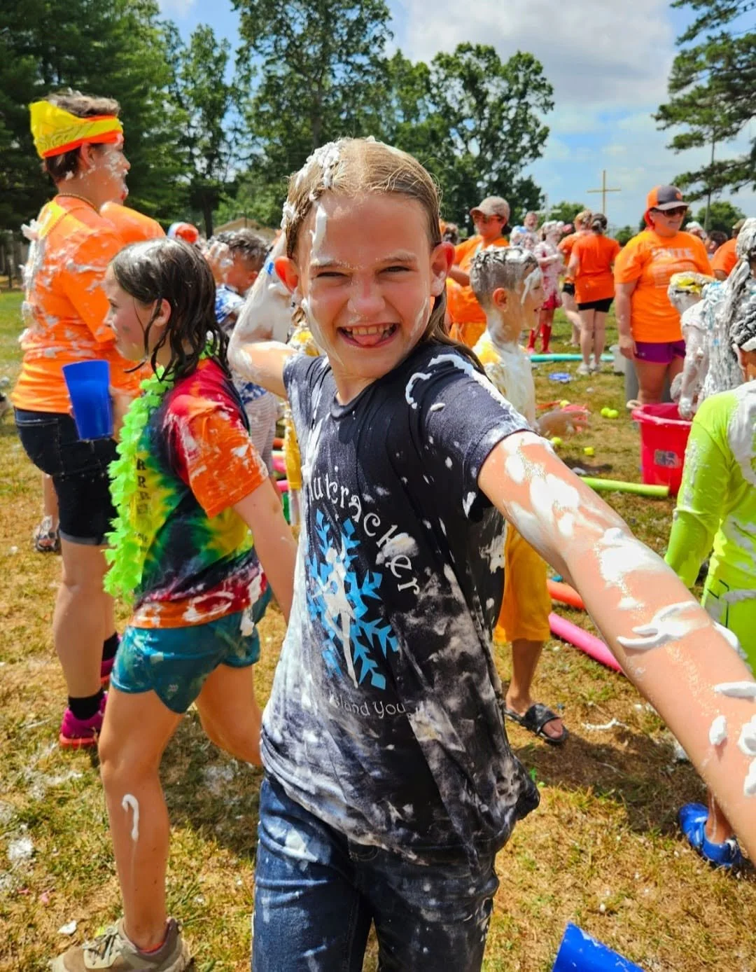 Children participating in a playful outdoor event with foam and water, smiling and enjoying themselves.