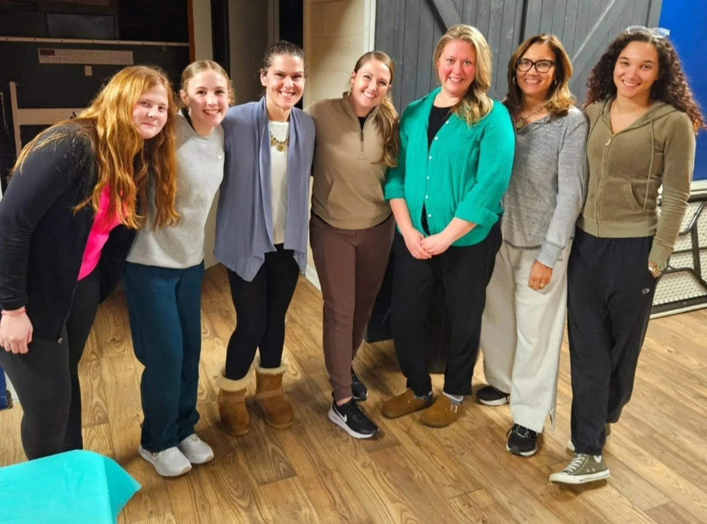 Group of eight women standing side by side indoors, smiling at the camera.