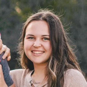 A smiling young woman with shoulder-length brown hair outdoors