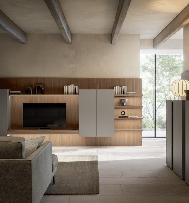 Interno di un soggiorno con parete attrezzata in legno, televisore, librerie con libri e decorazioni, grande finestra con vista su alberi verdi.