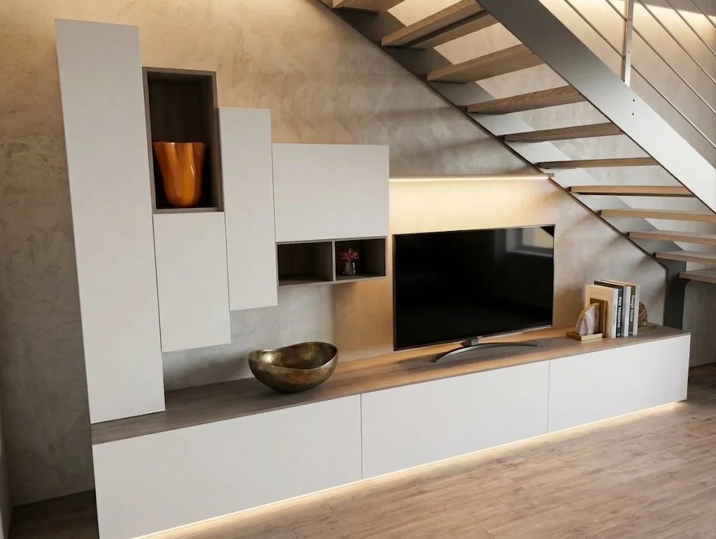 Ripiano passante con televisore, libri e decorazioni, sotto una scala a giorno in legno e metallo, e pareti con finitura in pietra o cemento.