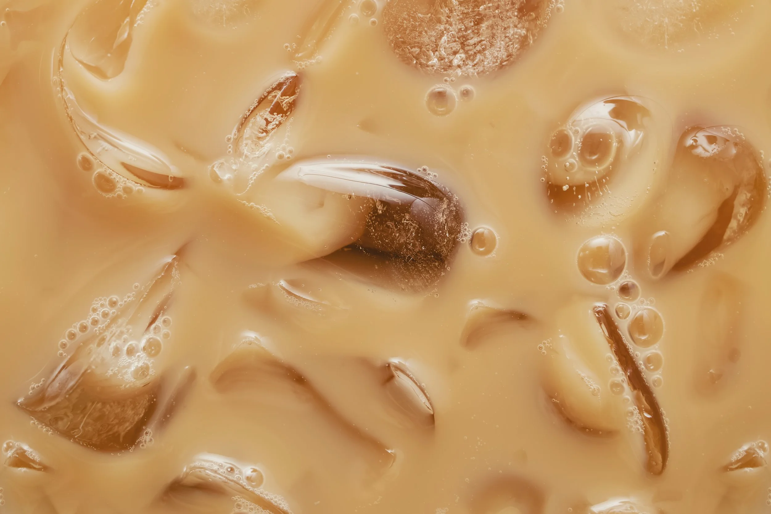 Close-up view of iced coffee with milk and ice cubes.
