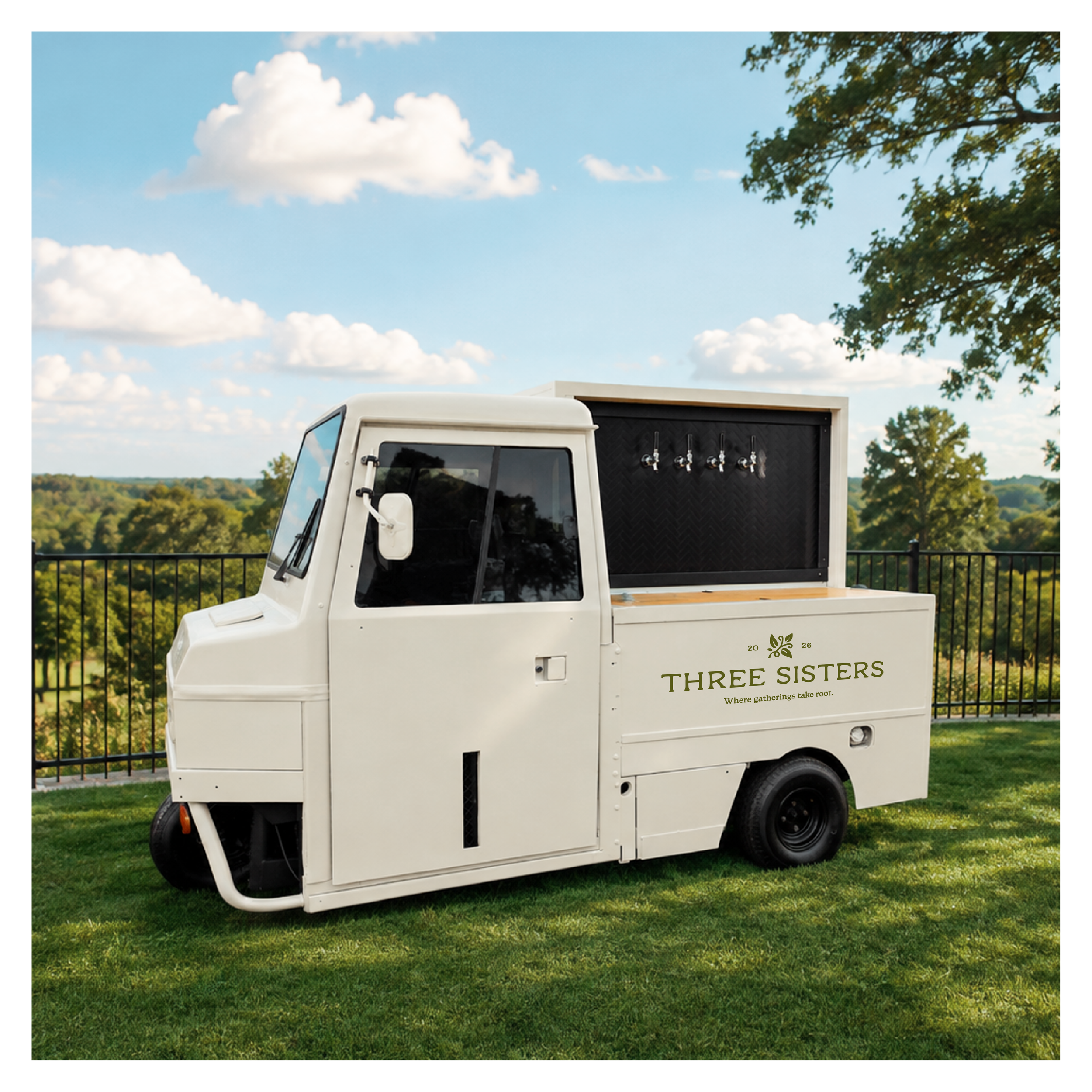 A white truck with a serving window and taps for beverage dispensing, parked on green grass under a partly cloudy blue sky with trees in the distance.