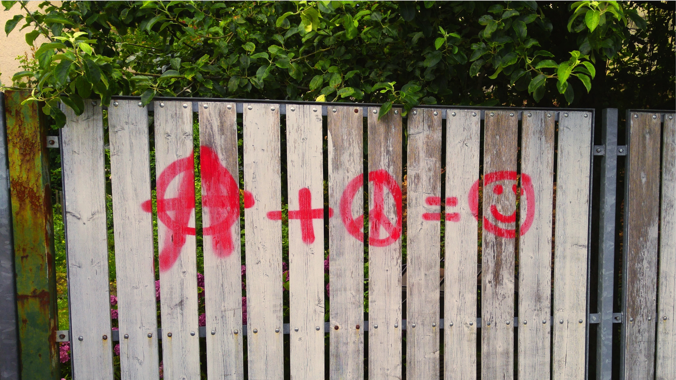 Graffiti on a wooden fence: anarchy symbol plus peace sign equals smiley face