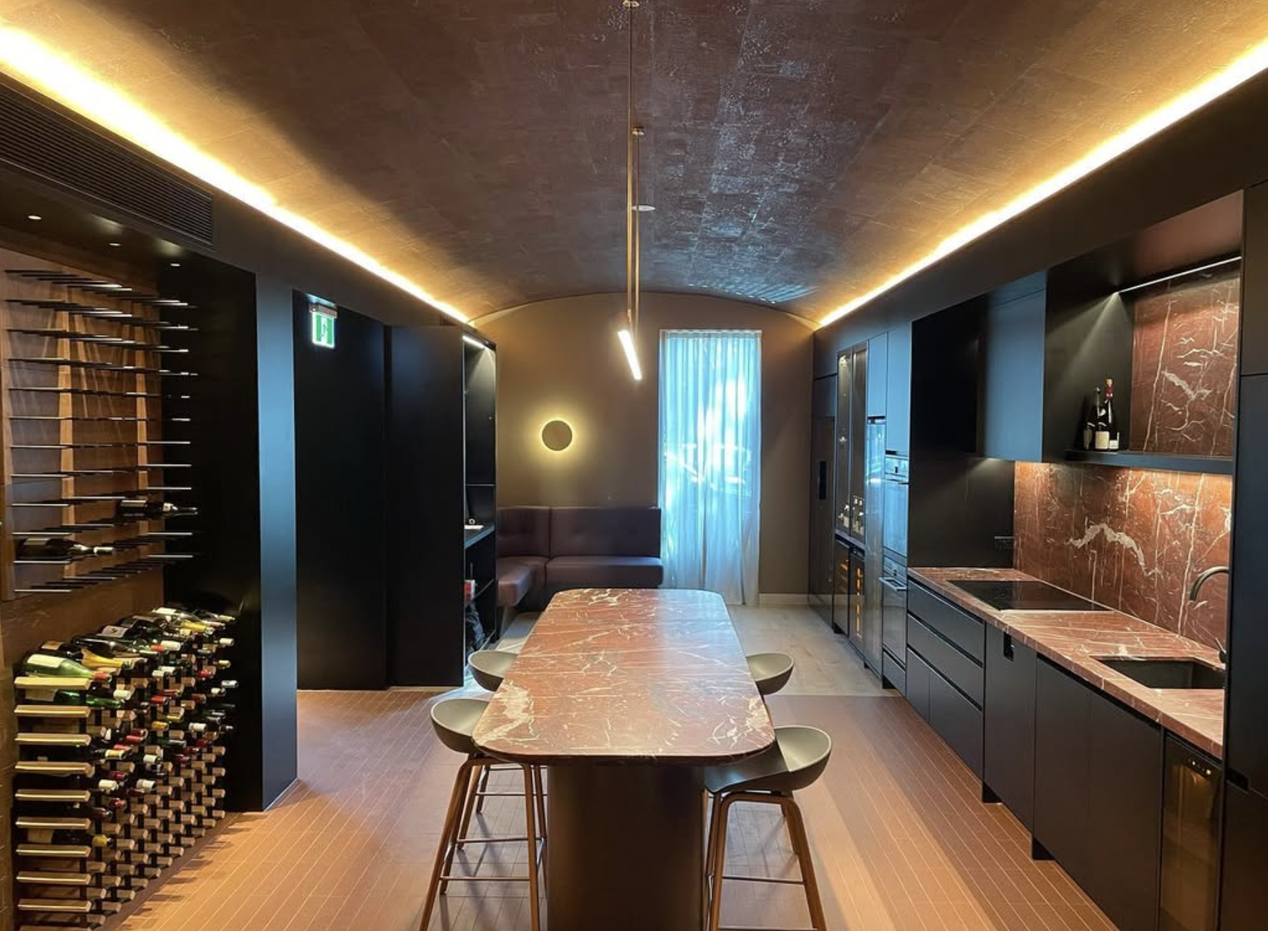 Modern kitchen with wine rack, marble table, black cabinetry, wine bottles, built-in appliances, and seating area.