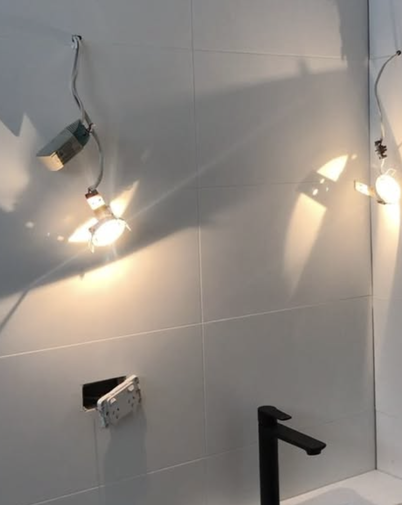 Ceiling with multiple installed spotlights casting bright light on the gray tiled wall below.