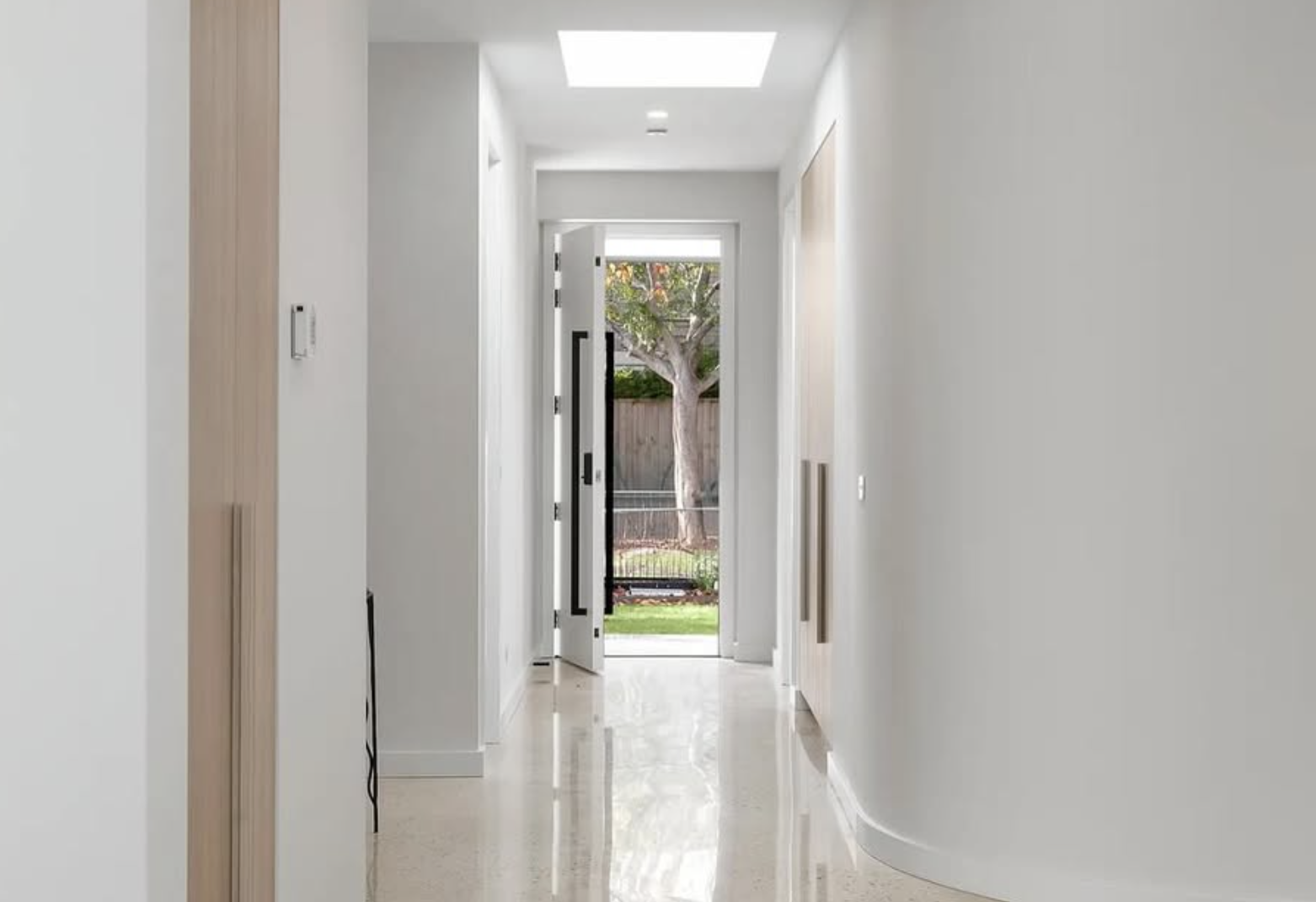 Bright hallway with an open front door revealing a yard with a tree and a wooden fence.