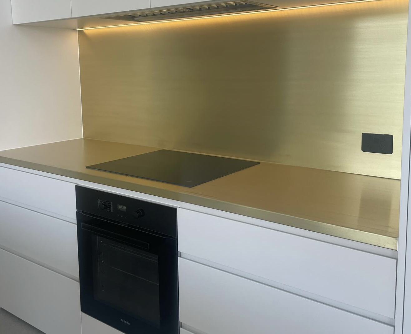 Modern kitchen with a built-in black oven, a flat induction cooktop, and a gold-colored backsplash with integrated lighting.