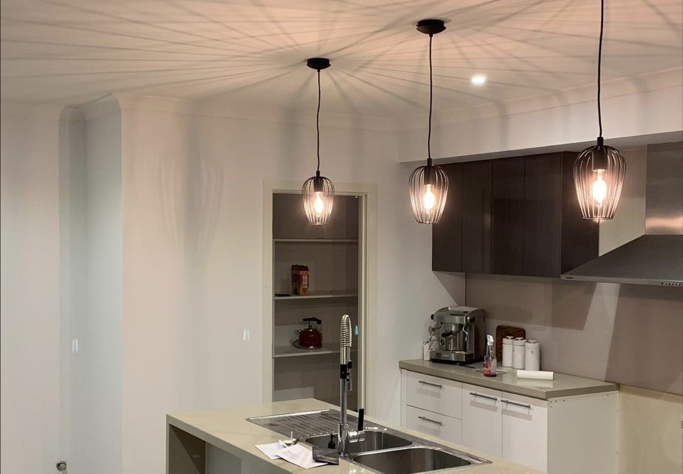 Modern kitchen with three hanging pendant lights, a kitchen island with a sink, and dark upper cabinets.