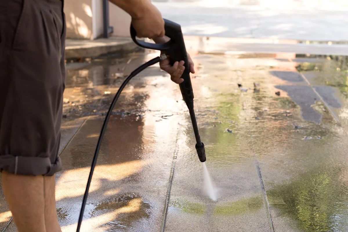 Person cleaning or washing a concrete or stone patio with a power washer.