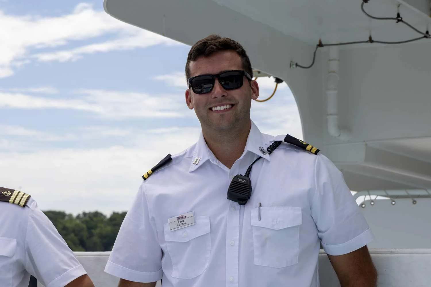 Pilot in uniform standing outside near a drone on a daytime with a partly cloudy sky.