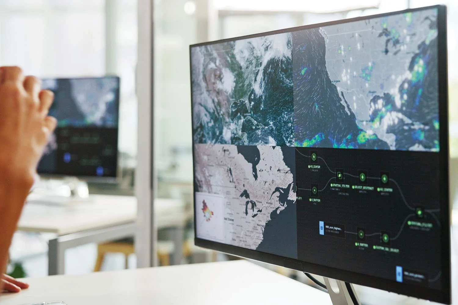 Computer monitor displaying weather patterns, geographic maps, and data routing networks.
