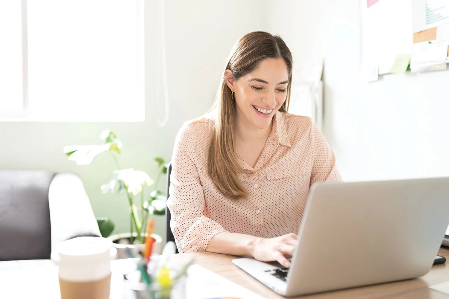 A woman sitting at a desk and smiling while looking at her computer screen.
