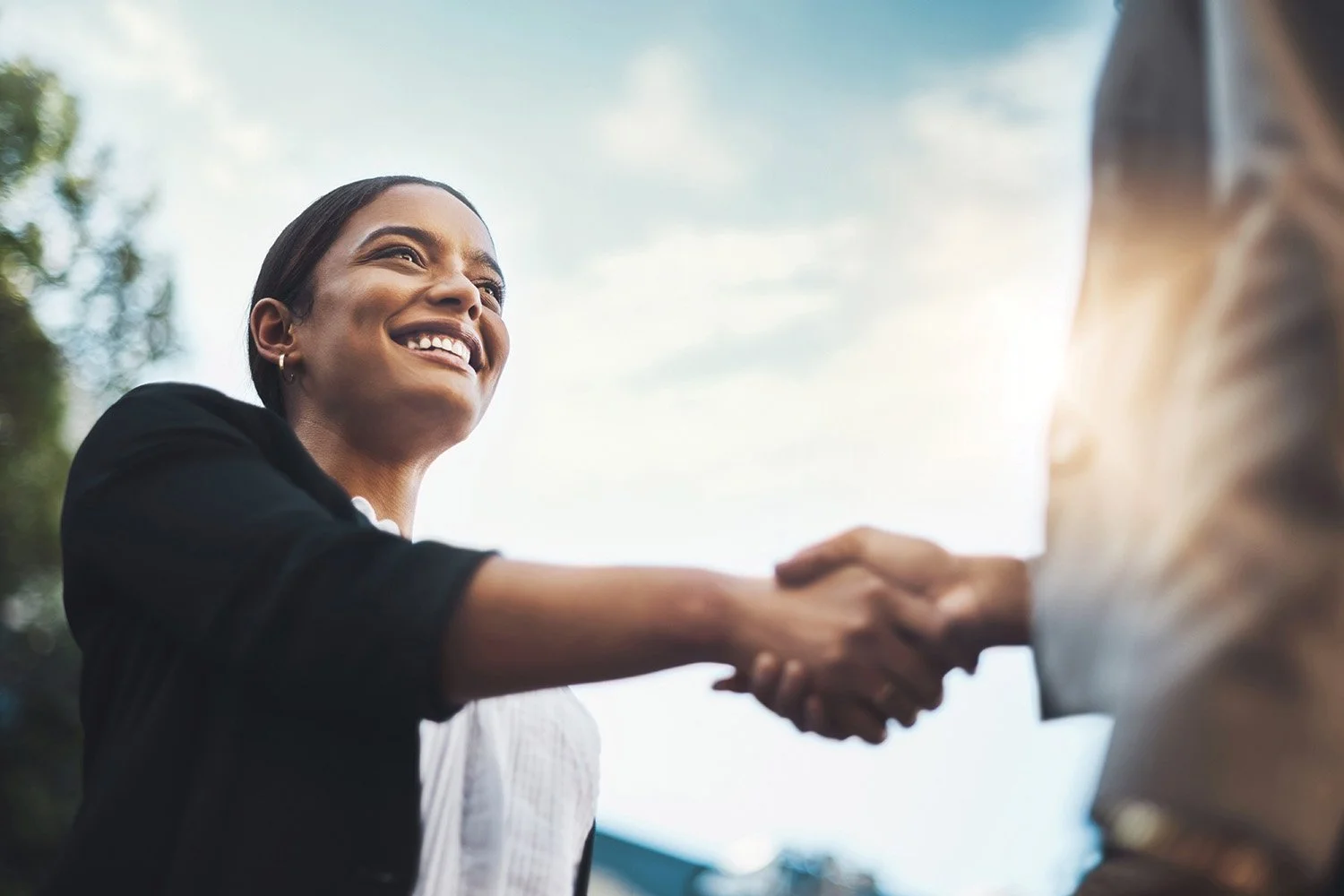 Two business professionals shaking hands in an office setting to symbolize a new partnership.