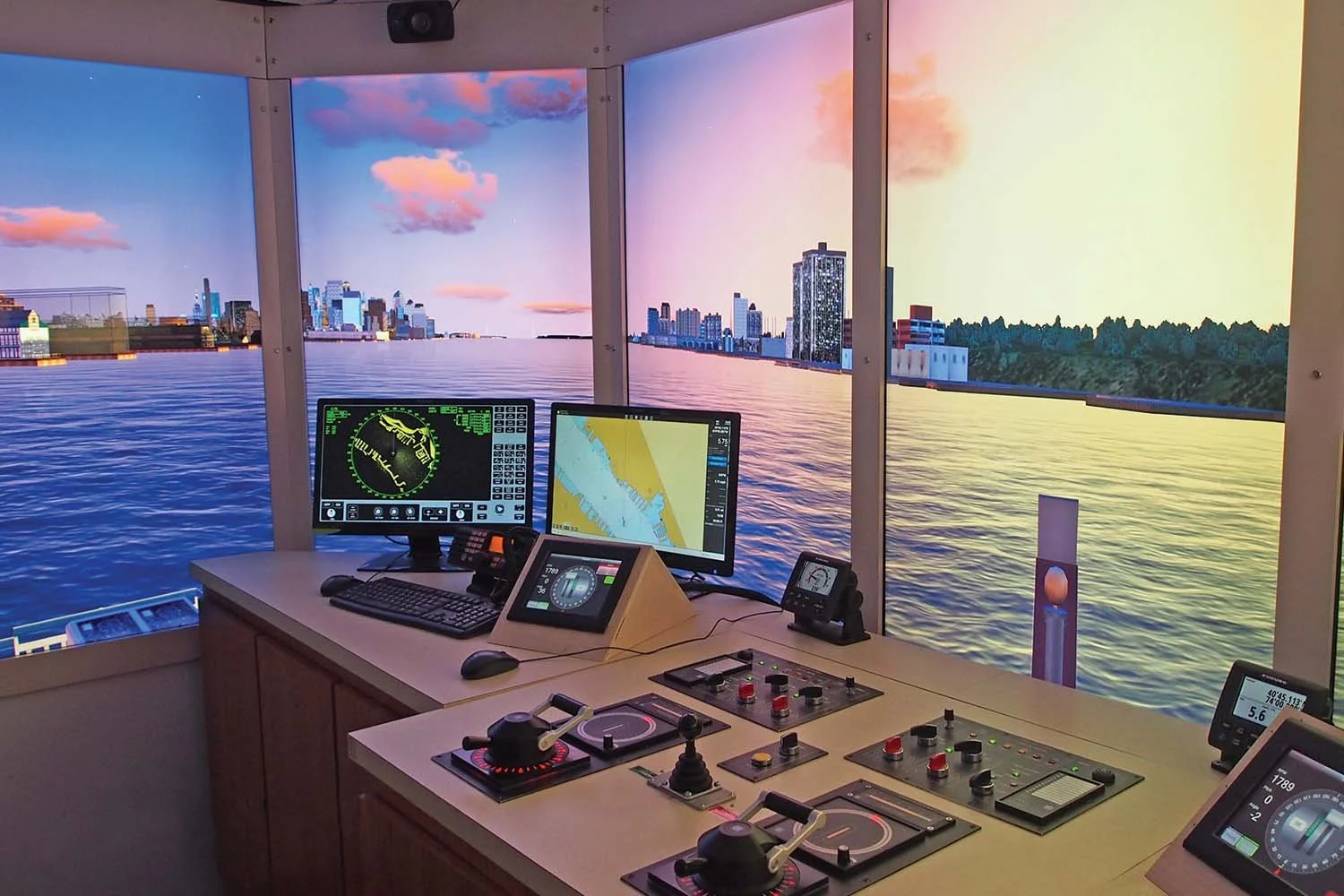 Navigation bridge simulator showing control consoles, navigation screens, and a scenic city skyline display.