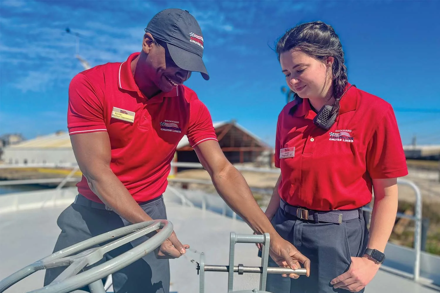 Two American Cruise Lines crew members operating deck equipment together outdoors.