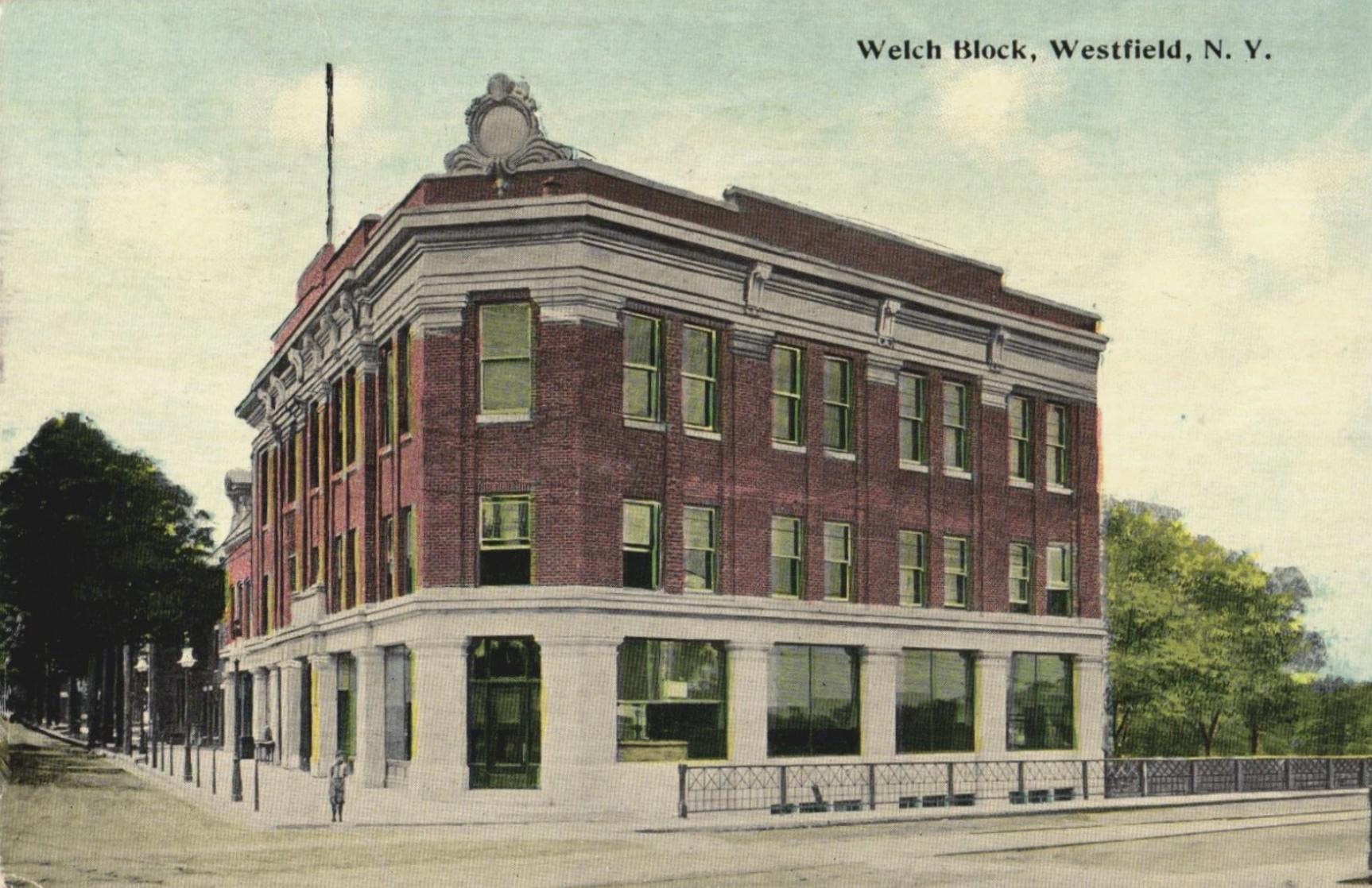 A multi-story brick building with white decorative trim at the top, large green-tinted windows, and a white base, located on Westfield, N.Y., with trees and a sidewalk in front.