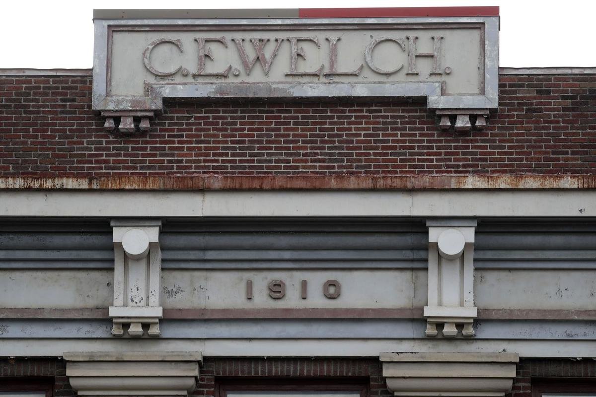 Close-up of a brick building with a sign that reads "C. E. WELCH" at the top and "1910" inscribed below.