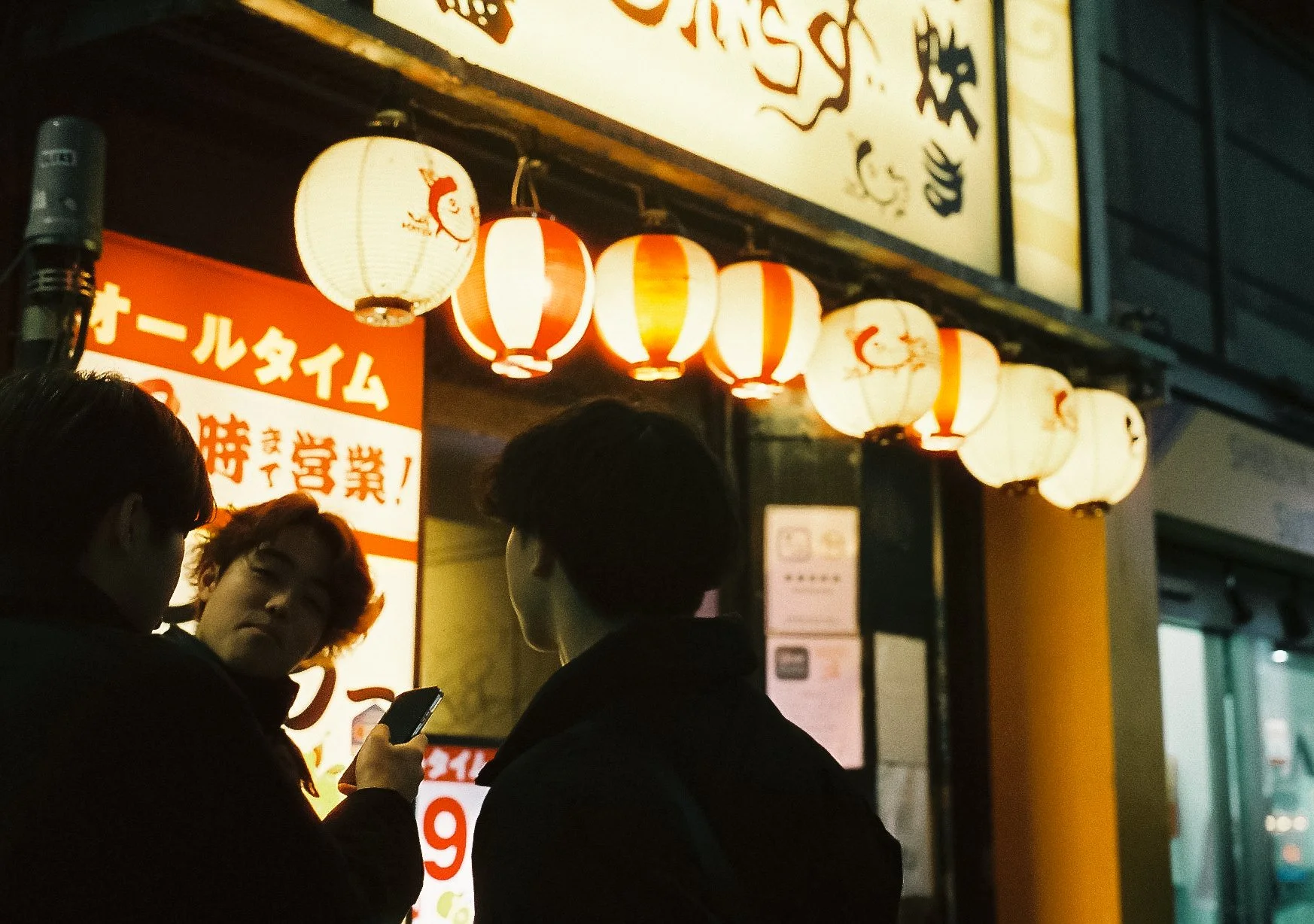 Warm glowing yellow paper lanterns hanging outside a traditional Japanese restaurant at night.
