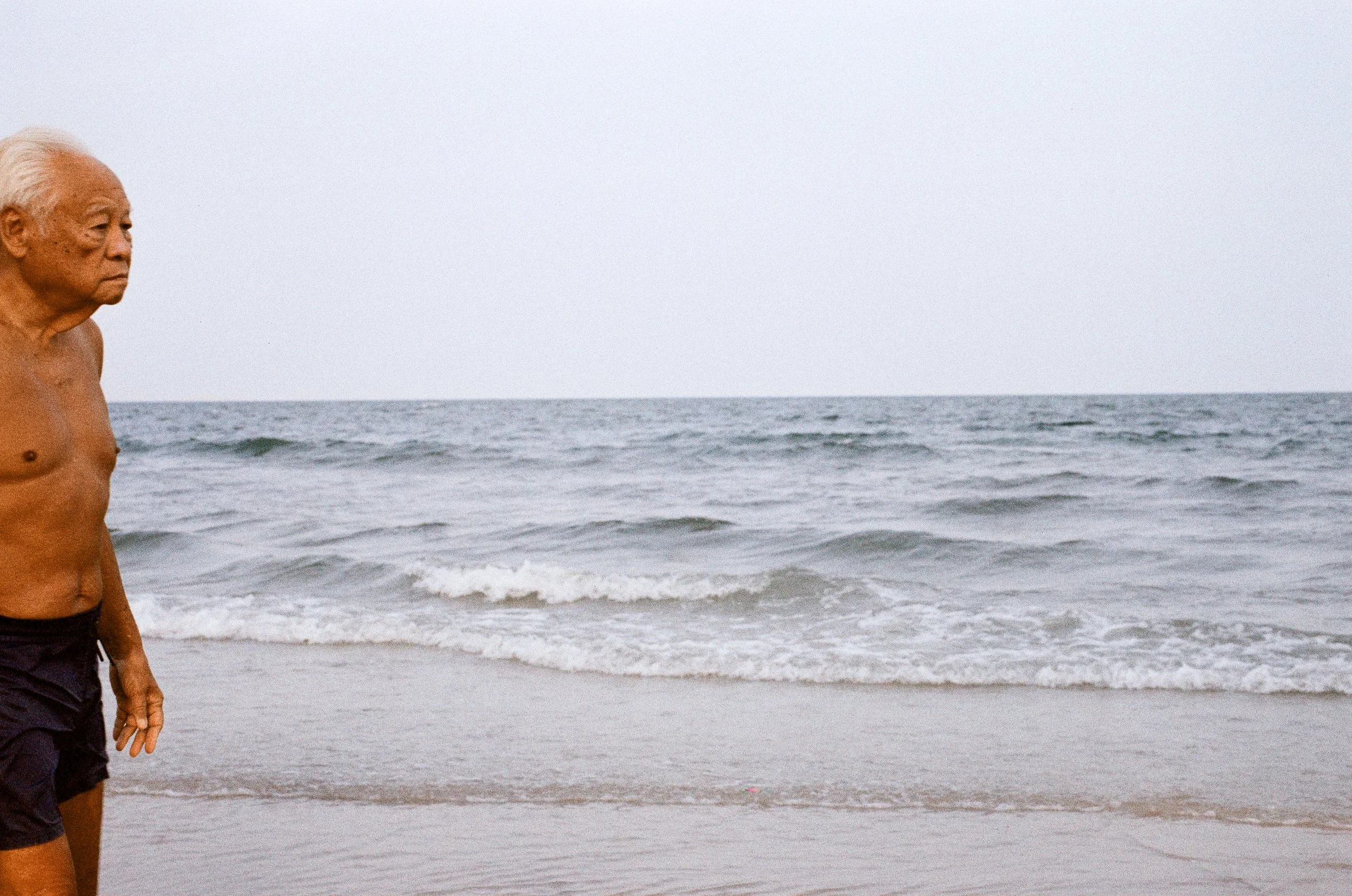 candid photography of an old men on the beach at Hua Hin, Thailand showing the sea and sand photography using a leica film photography 