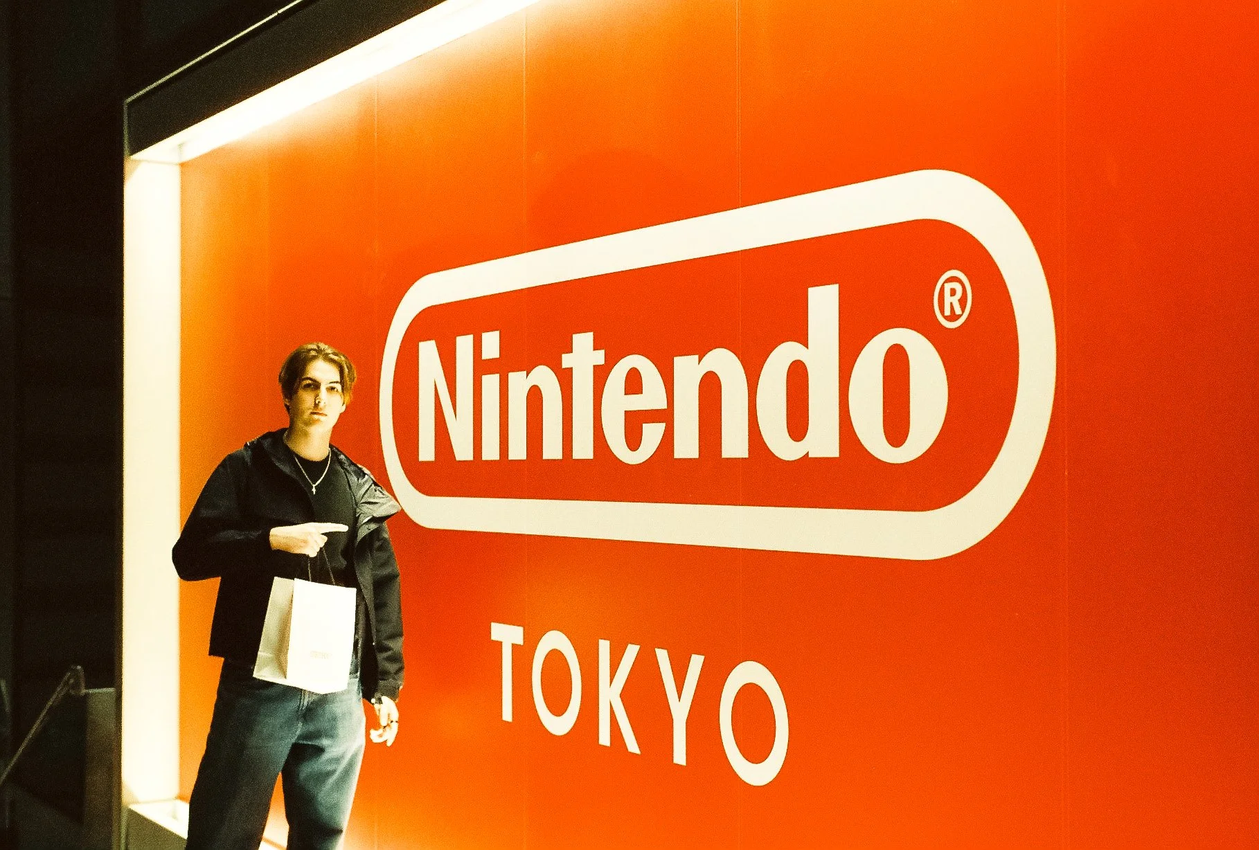 Bright orange Nintendo Tokyo store sign with a shopper standing in front.